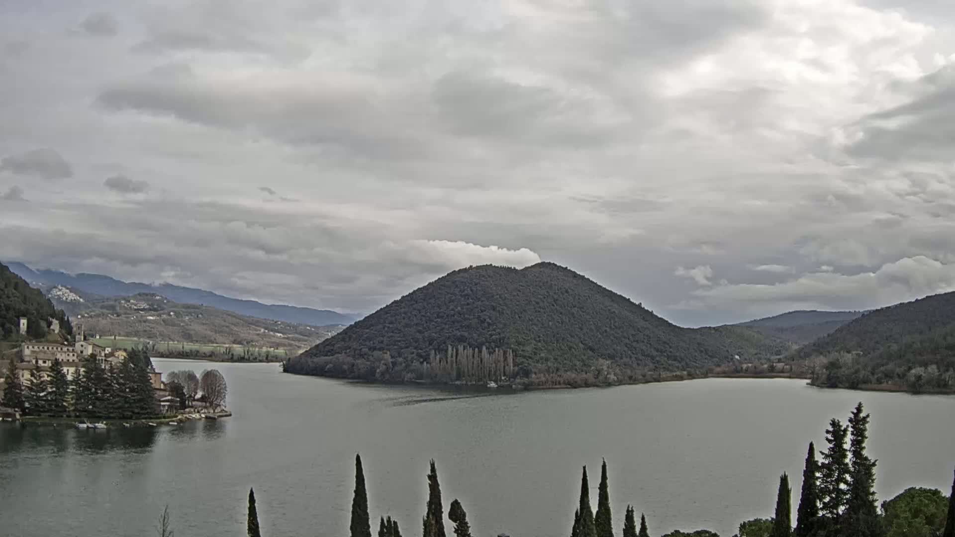 A lake surrounded by hills and a village under an overcast sky.