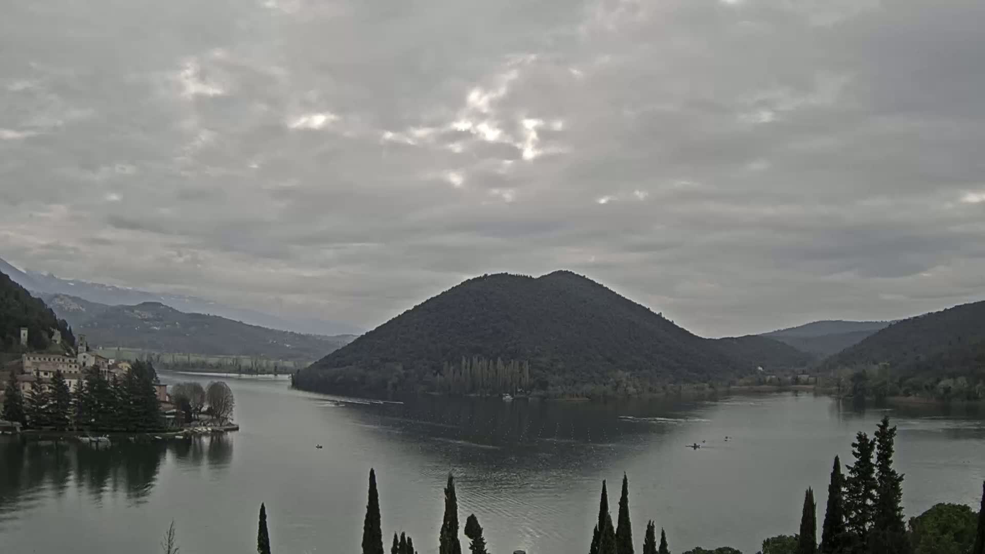 A calm lake is nestled between dark green hills under a cloudy sky.