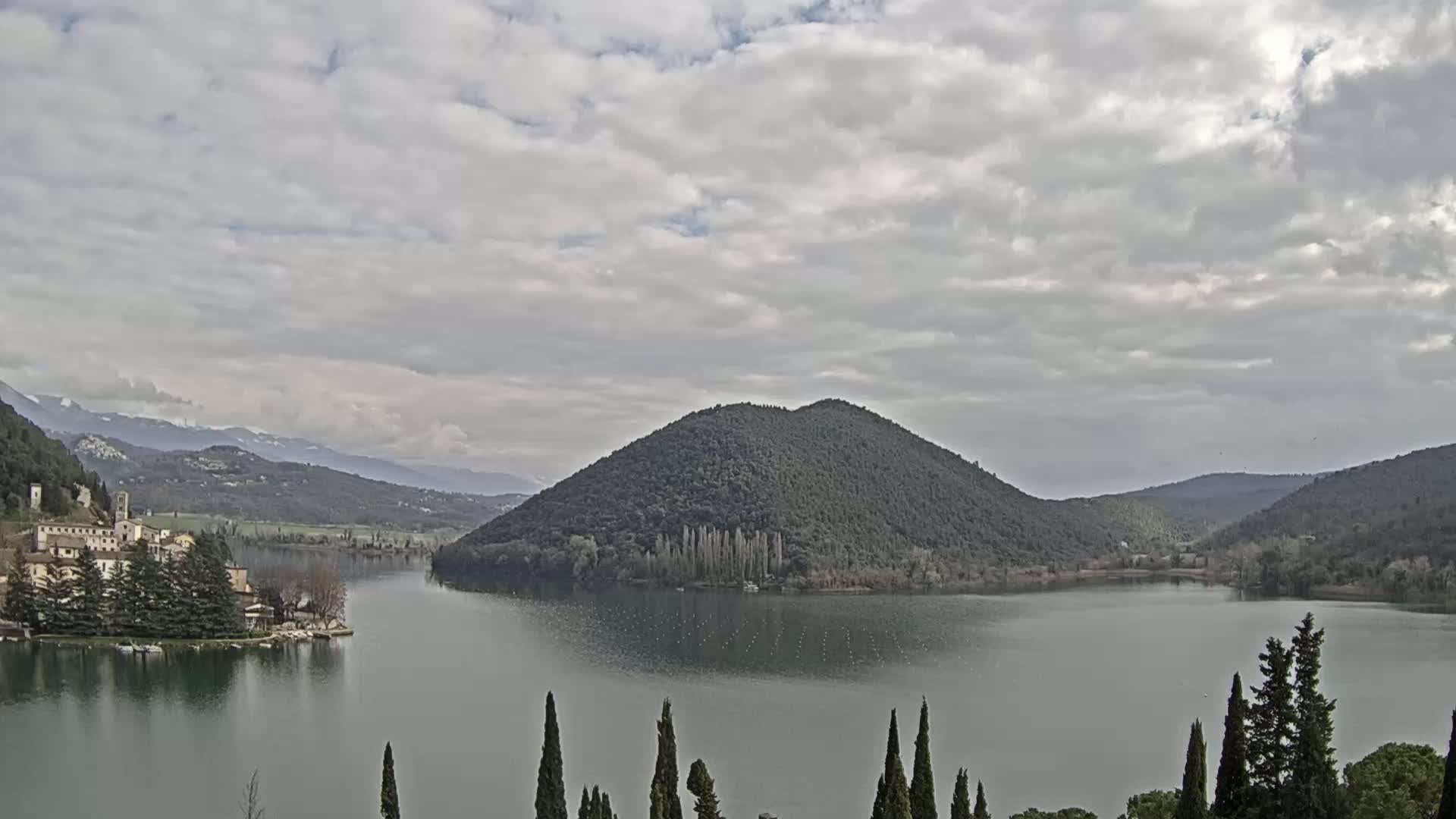 A lake surrounded by hills and a village under a cloudy sky.
