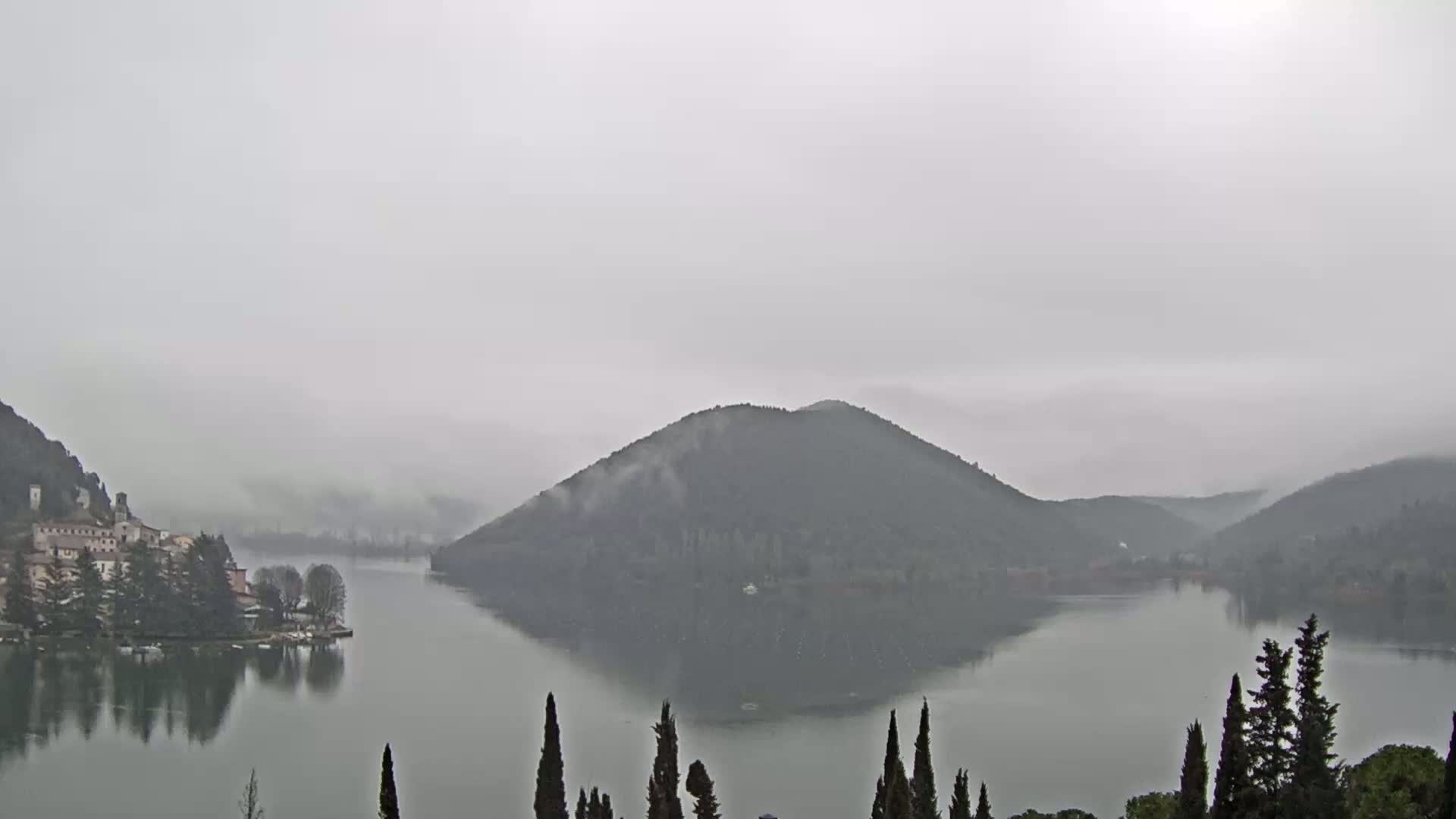 A calm lake is surrounded by fog-covered hills and a small village on the left shore.