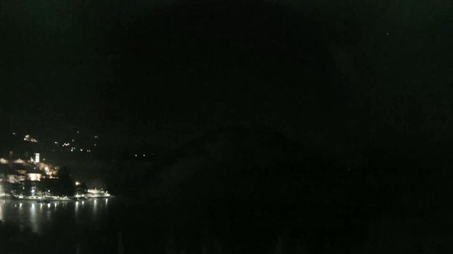 A nighttime view shows a body of water reflecting the lights of a town nestled on a hillside.