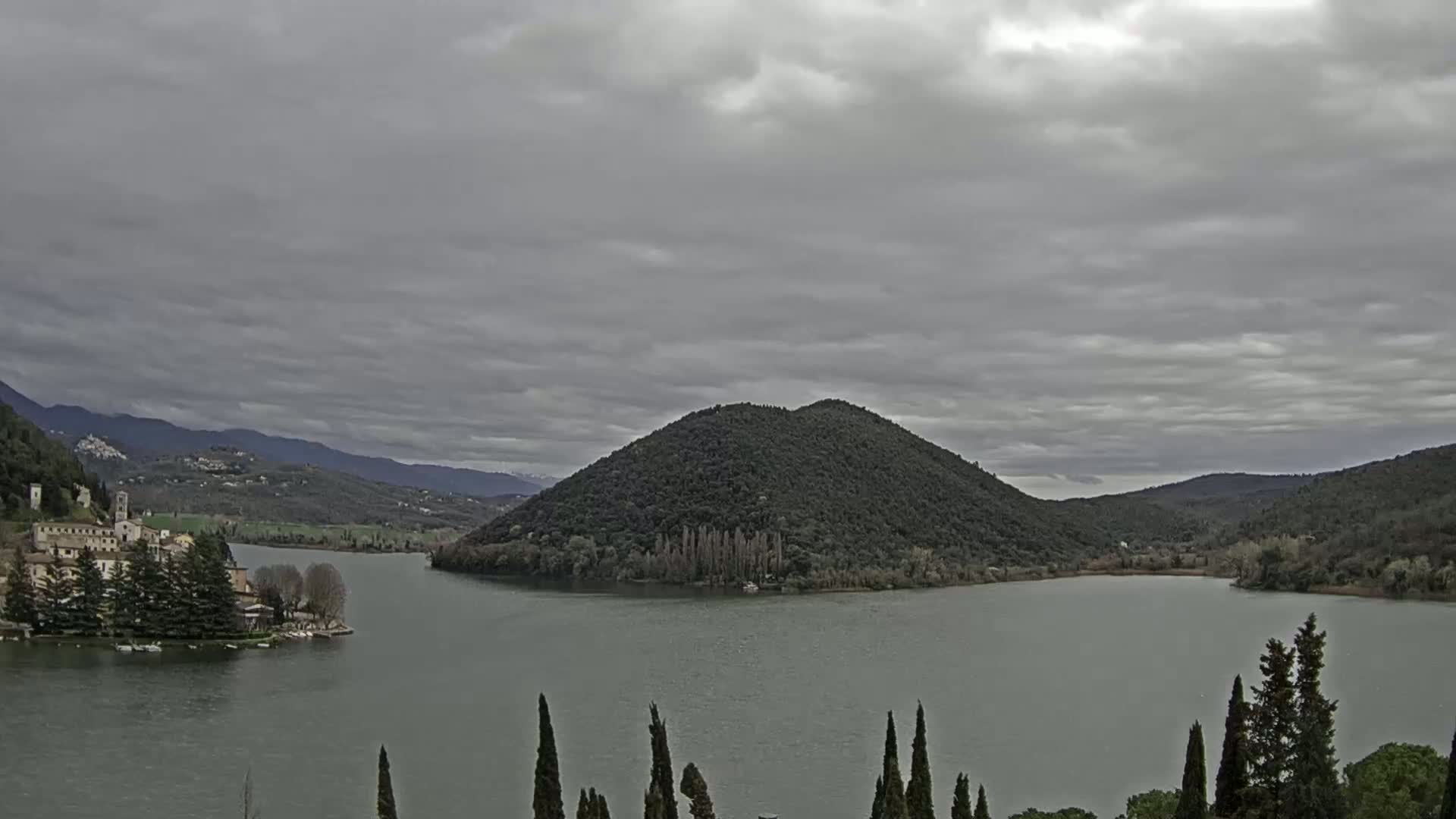 A lake surrounded by mountains and trees under an overcast sky.