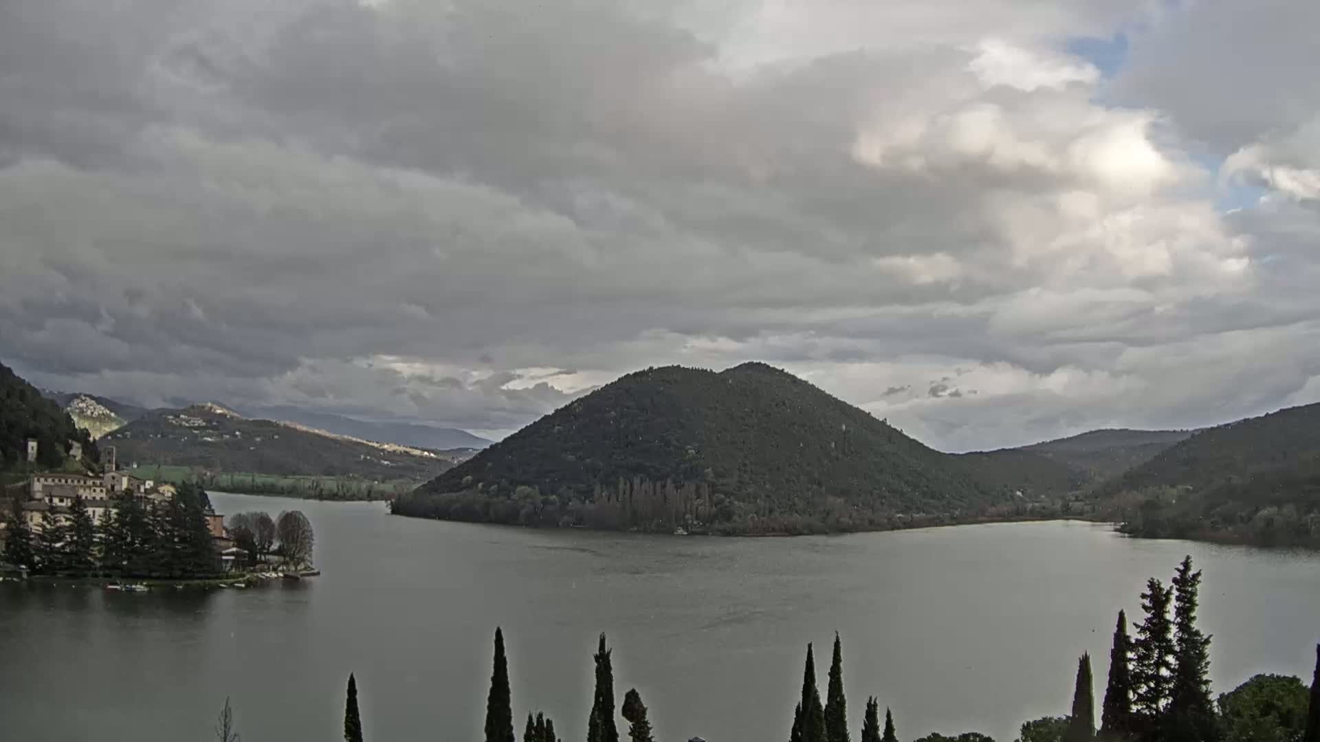 A lake surrounded by hills and a village under a cloudy sky.