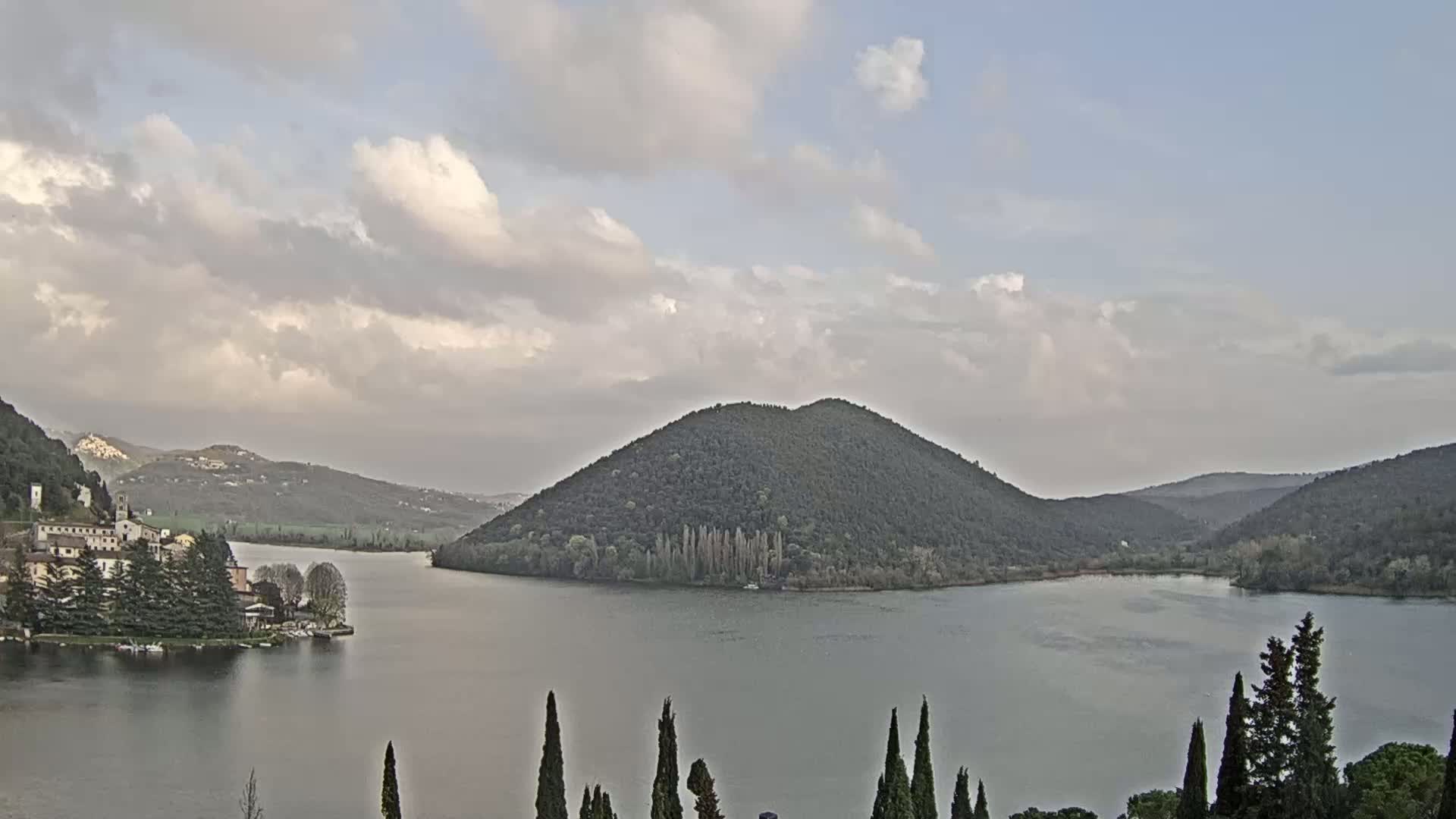 A lake surrounded by hills and a small town under a partly cloudy sky.