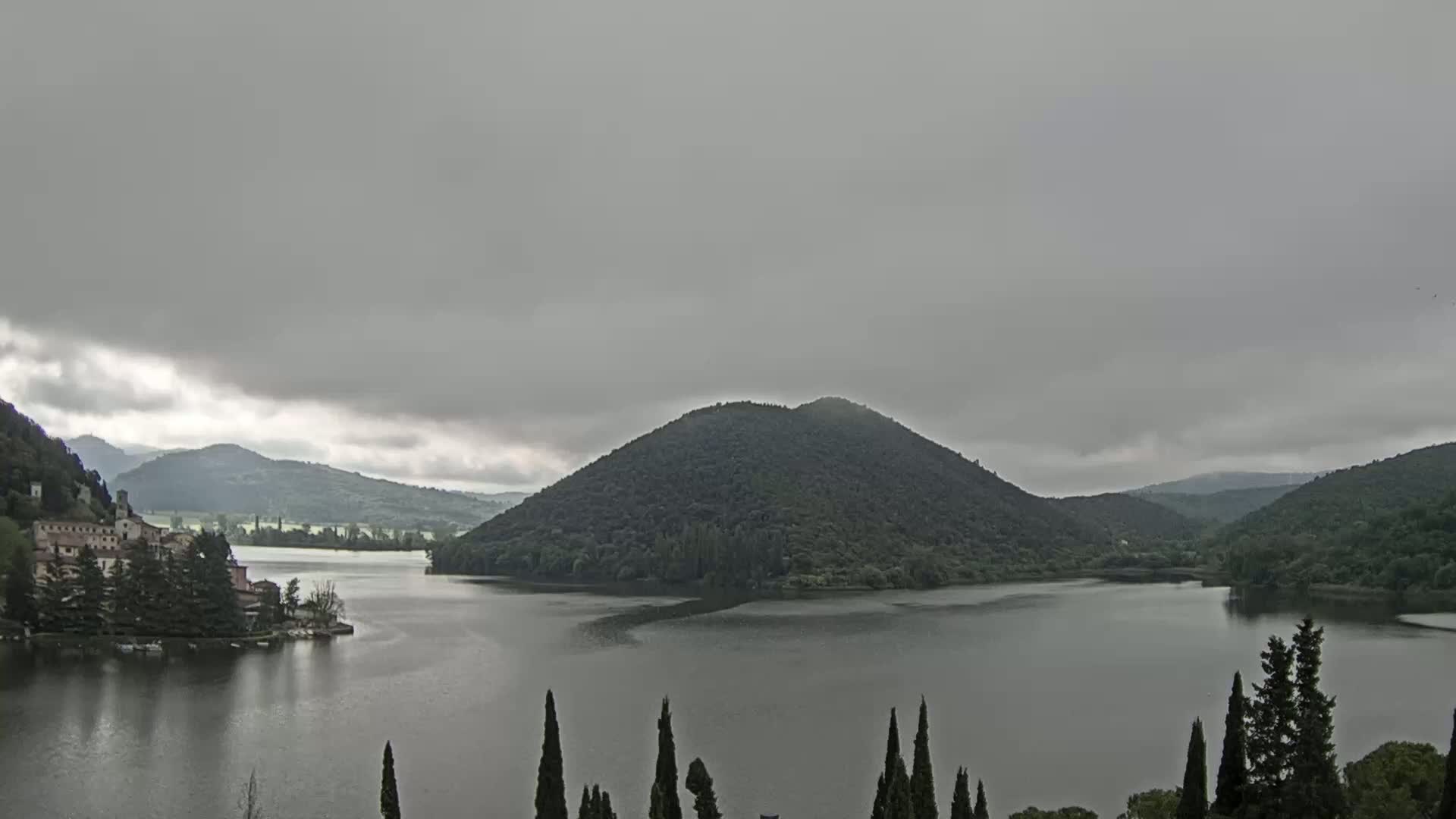 A lake is nestled between tree-covered hills under an overcast sky.