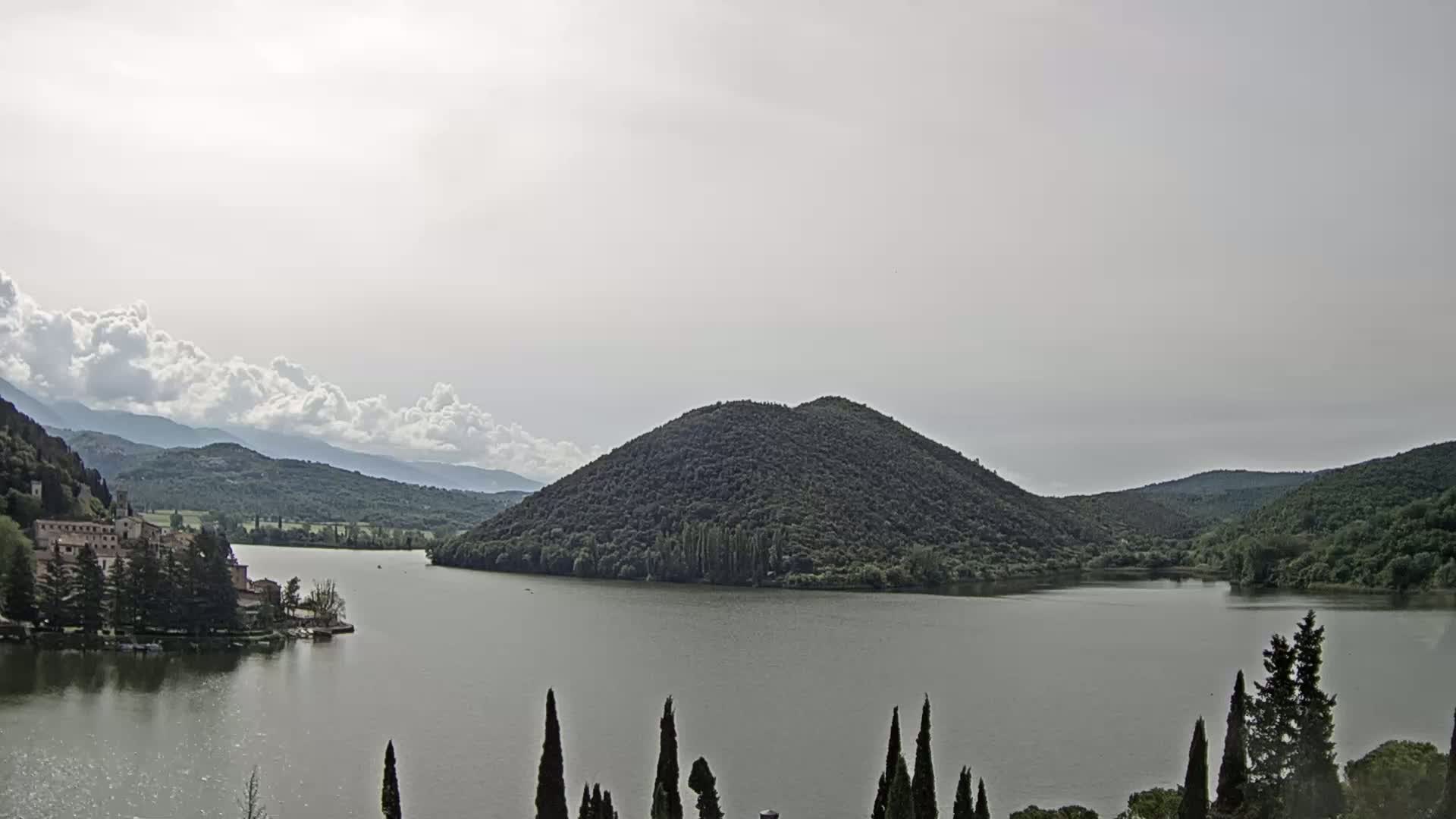 A lake is nestled between tree-covered hills under a partly cloudy sky.