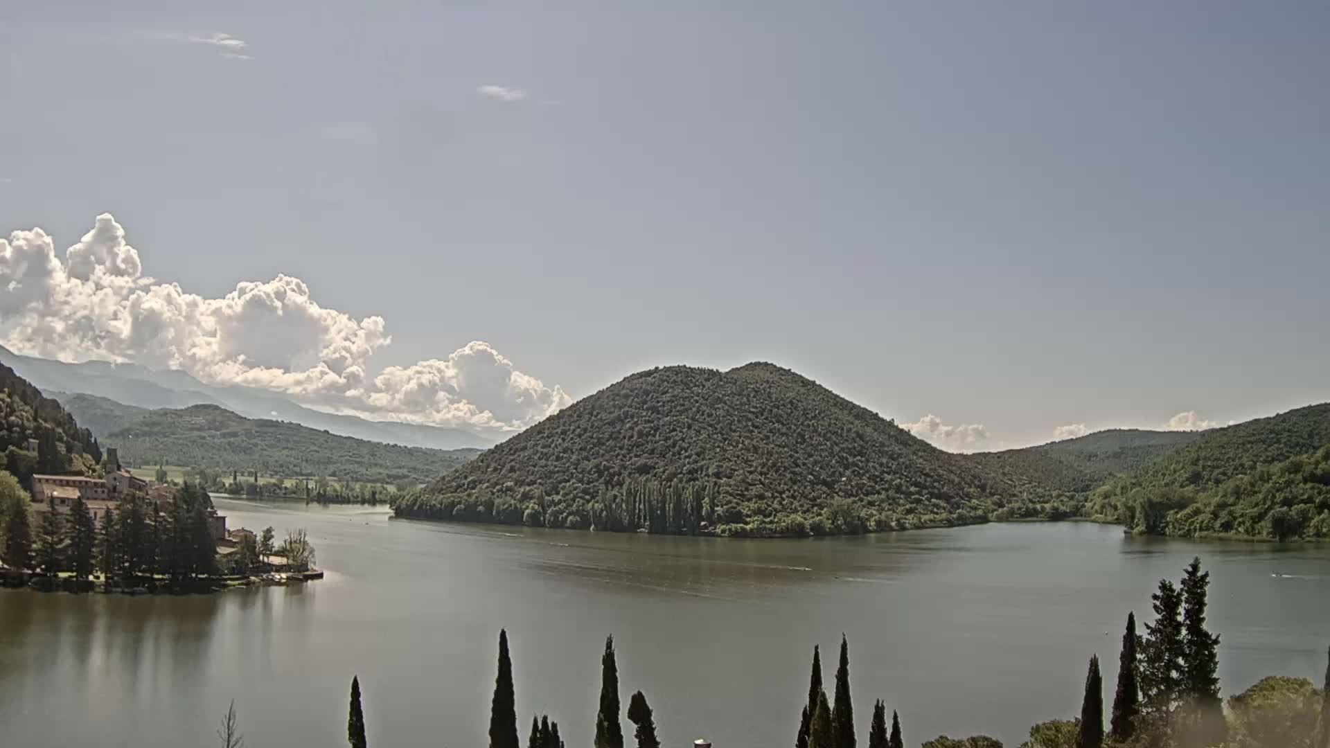 A lake is surrounded by green hills and mountains under a partly cloudy sky.