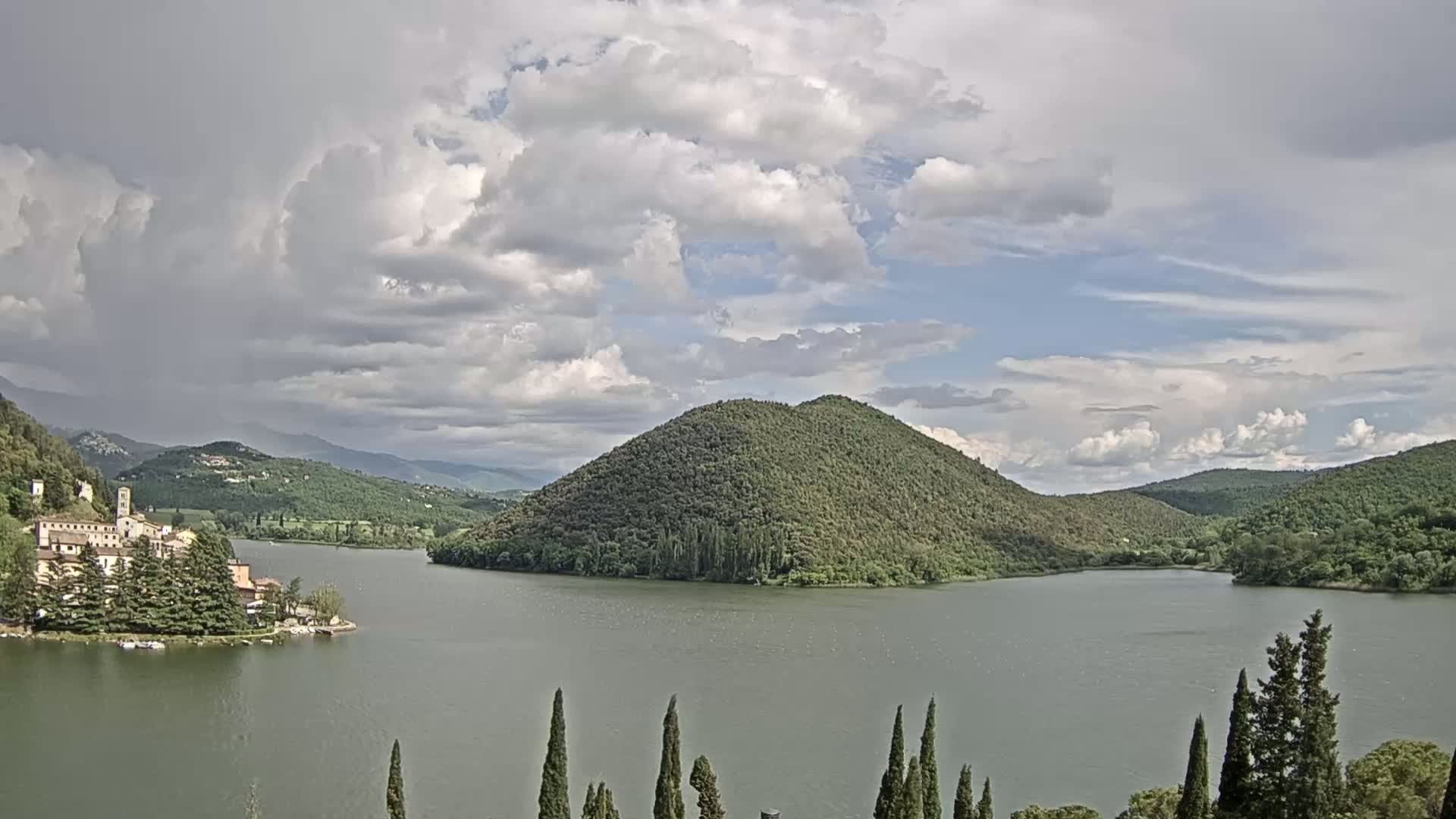 A lake surrounded by lush green hills and a small village under a partly cloudy sky.