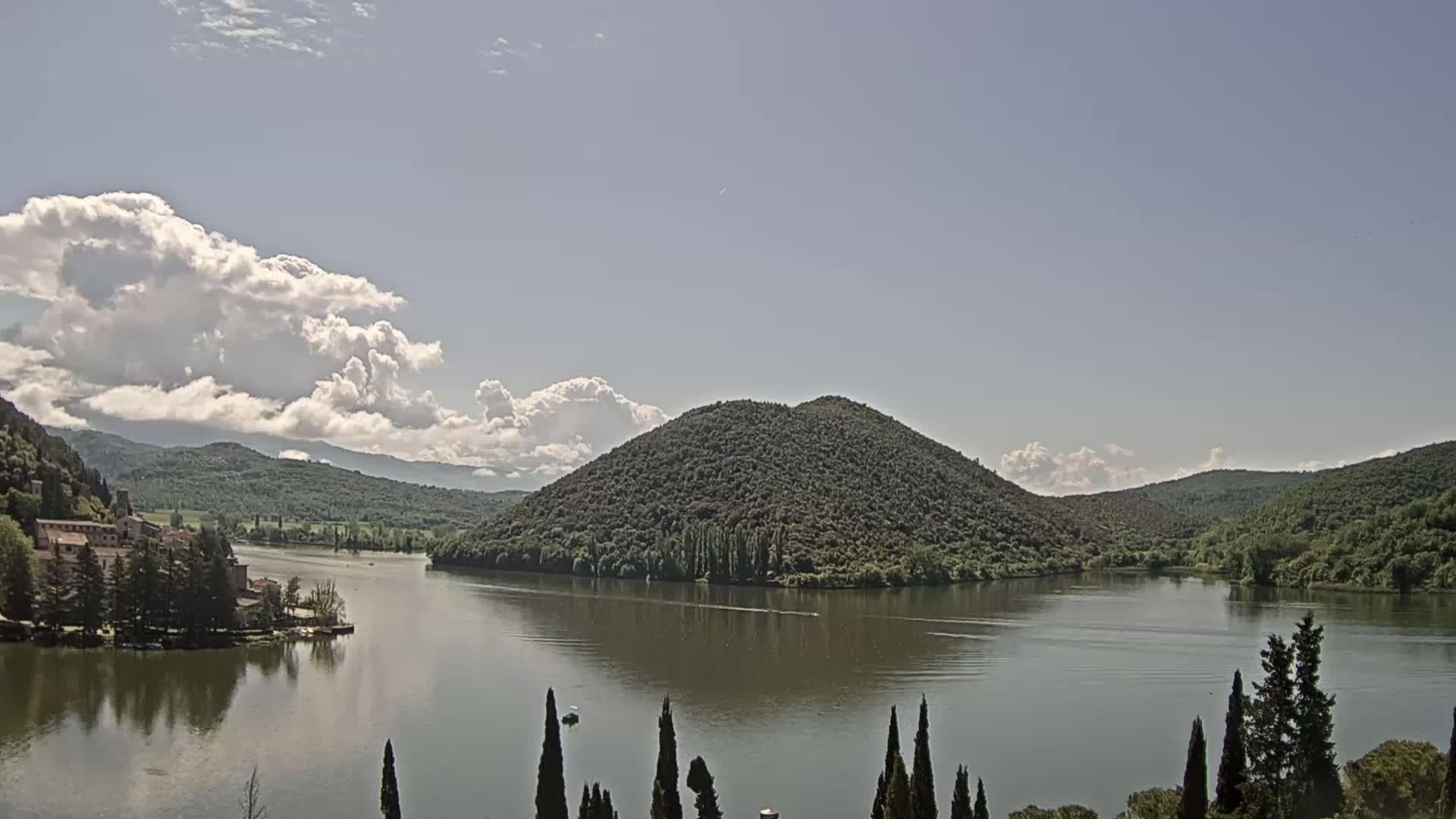 A calm lake is surrounded by lush green hills and a partially cloudy sky.