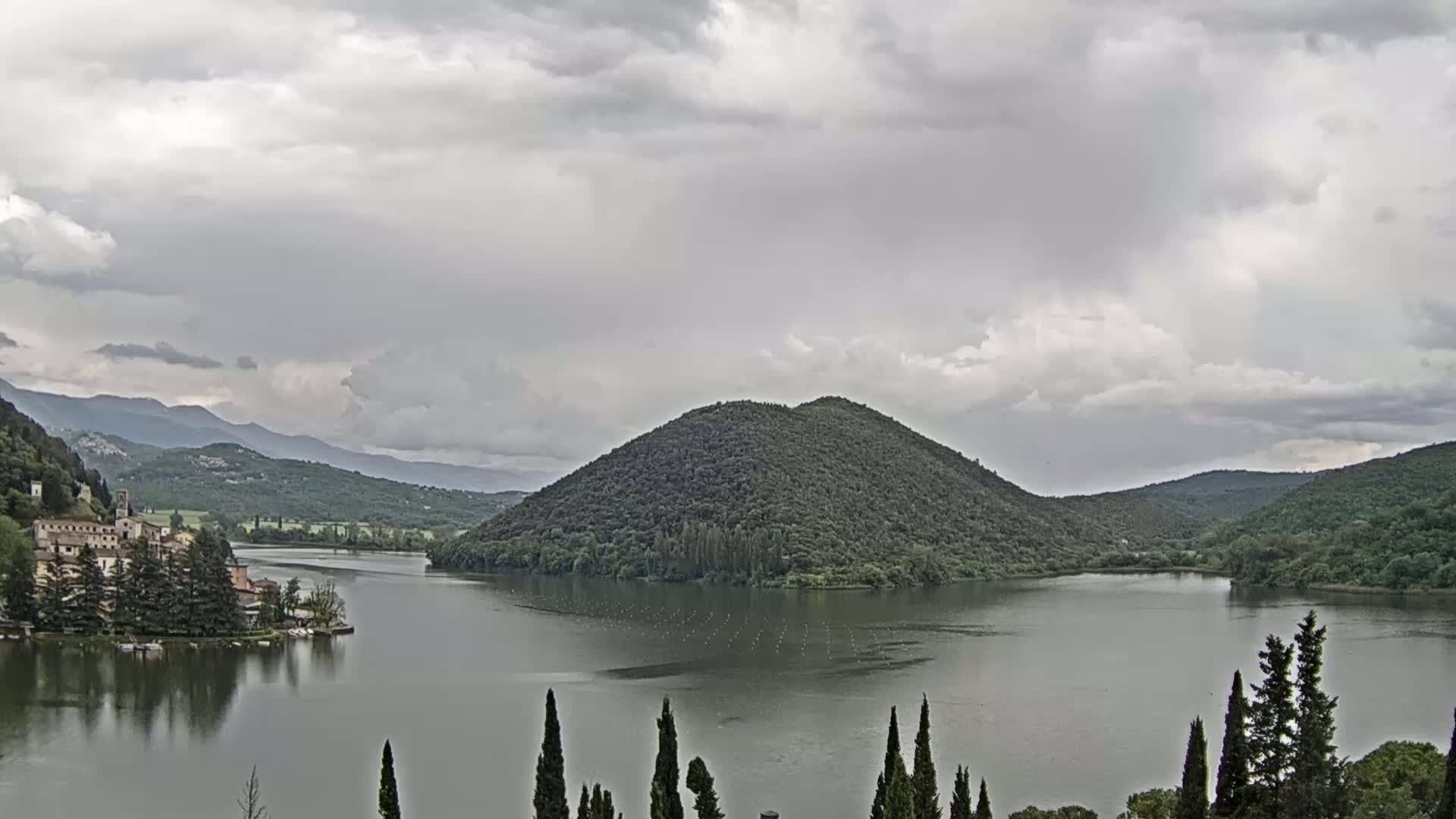 A lake surrounded by green hills and a village under a cloudy sky is visible.