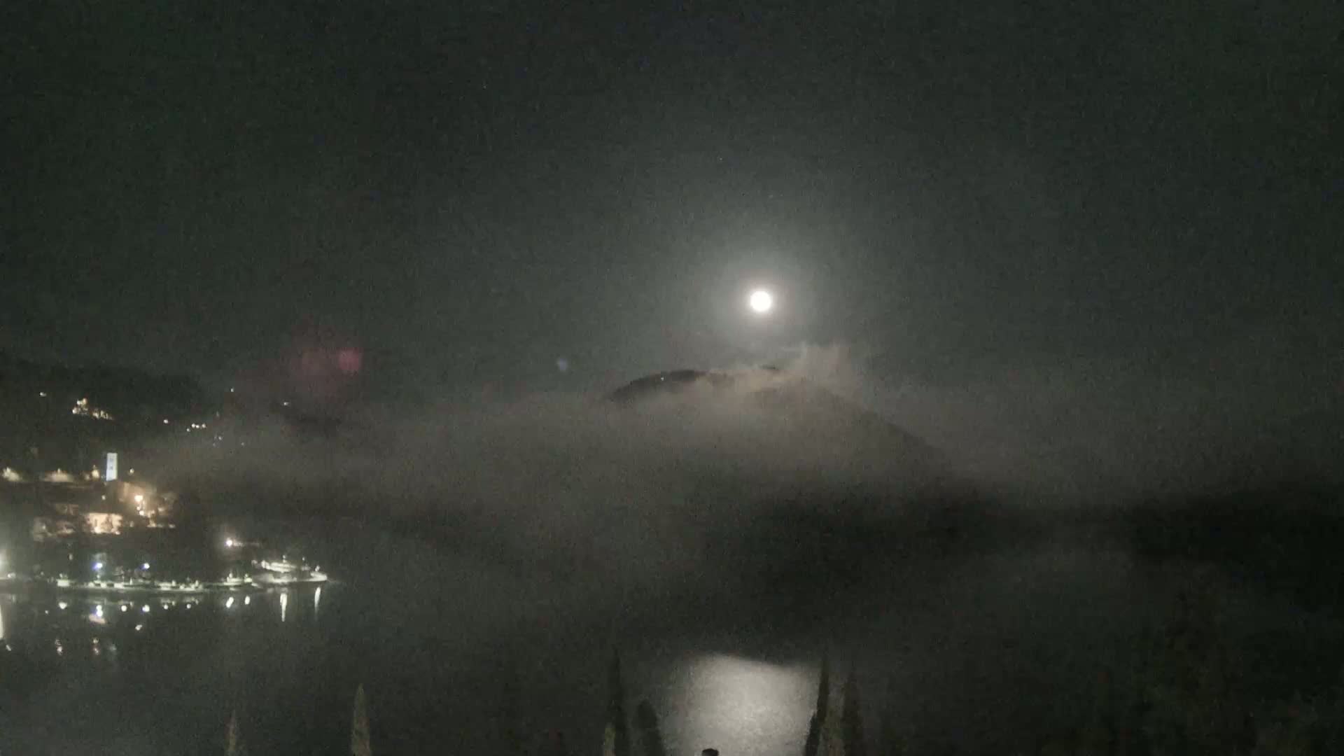 A bright moon shines over a foggy lake and hills at night.