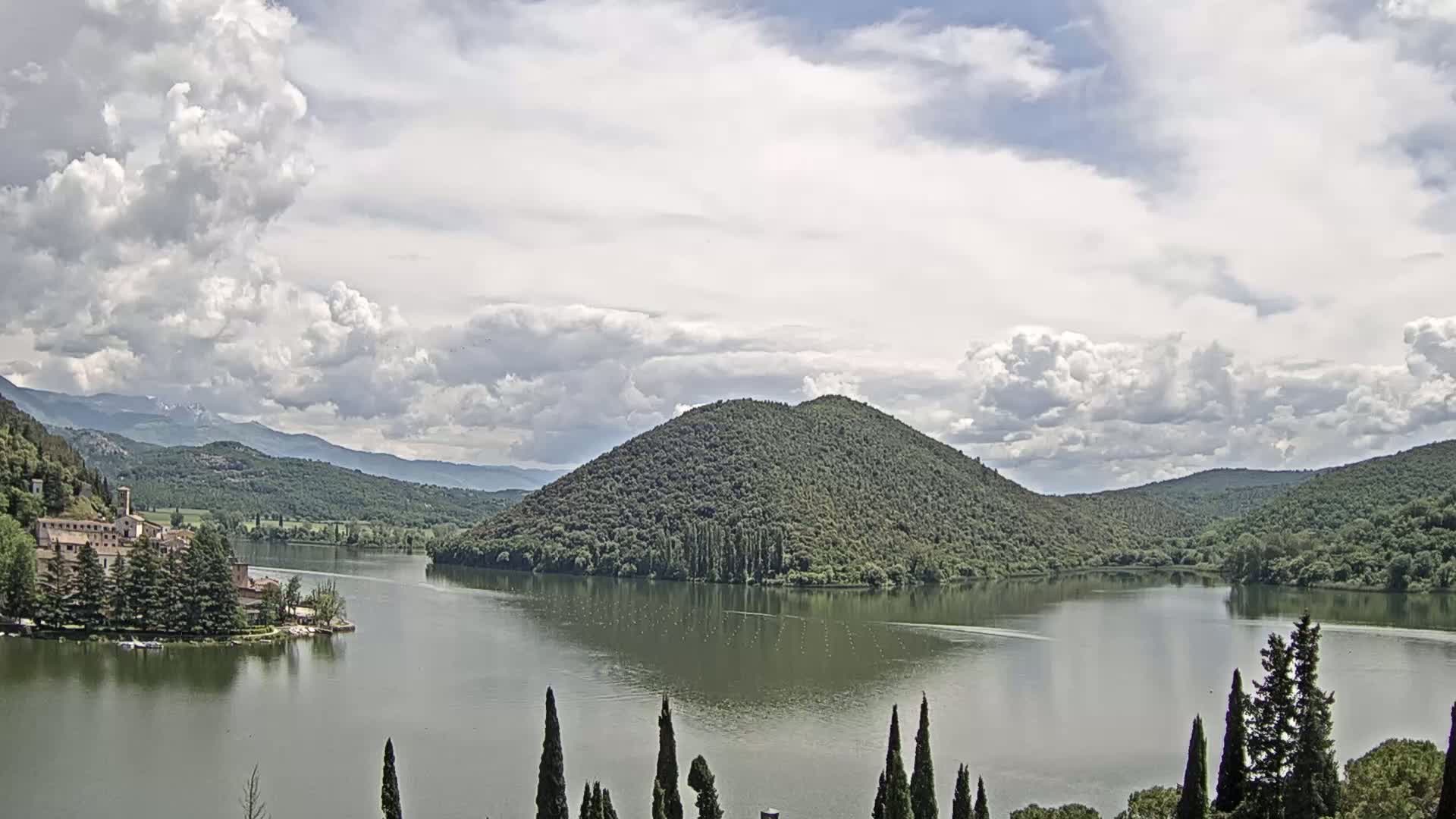 A lake surrounded by green hills and a building on the lakeshore under a partly cloudy sky.