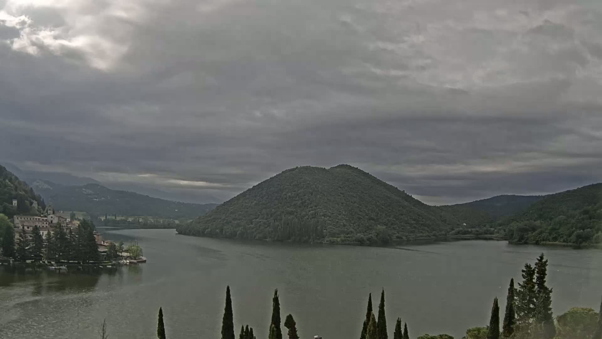 A lake surrounded by green hills and a village under an overcast sky.
