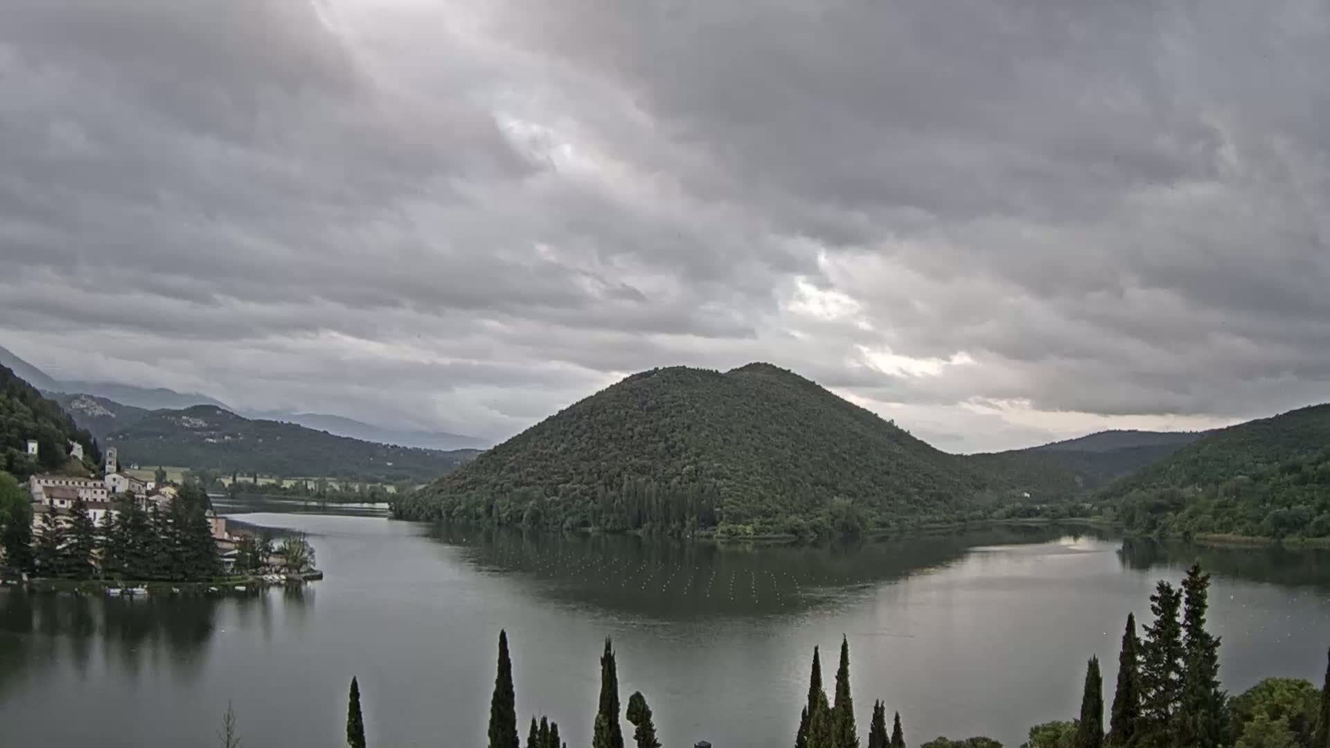 A lake surrounded by lush green hills and a small village under an overcast sky.