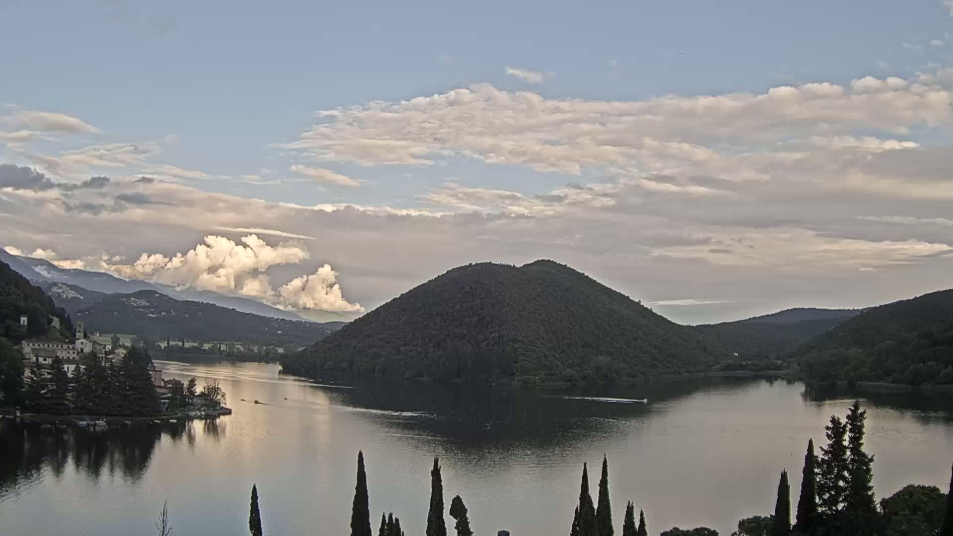 A calm lake is nestled among rolling hills under a partly cloudy sky.