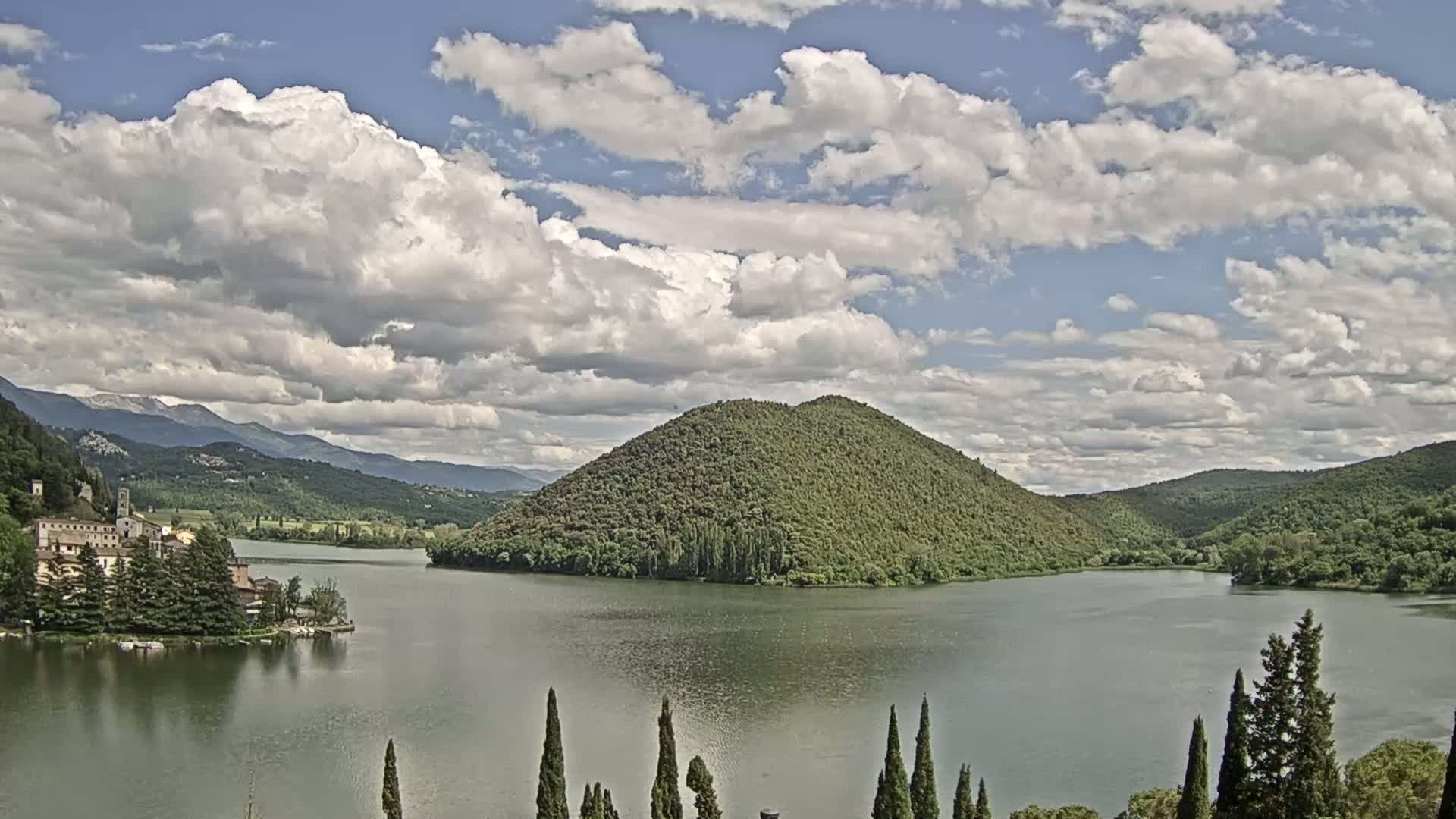 A lake surrounded by green hills and a village under a partly cloudy sky.