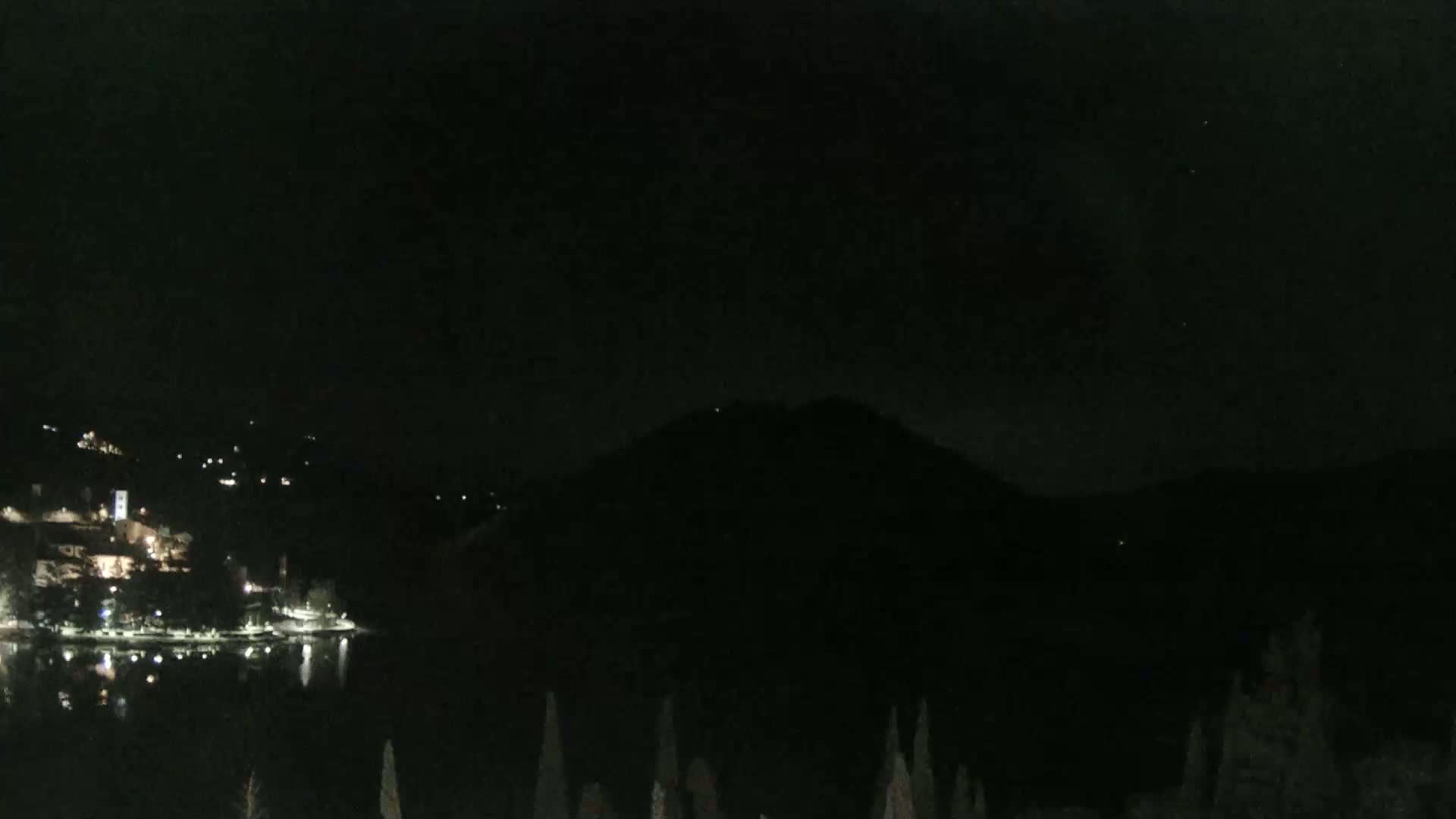 A nighttime view of a calm lake reflecting the lights of a town nestled against a dark mountain.