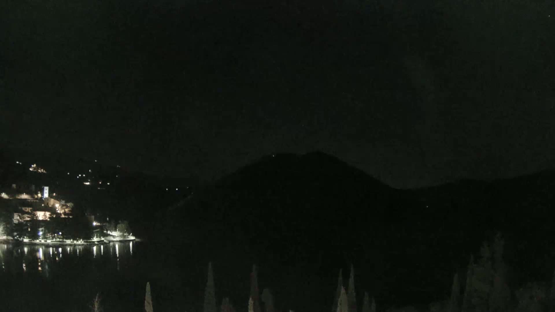 A nighttime view of a calm lake reflecting the lights of a town nestled at the base of a dark mountain.