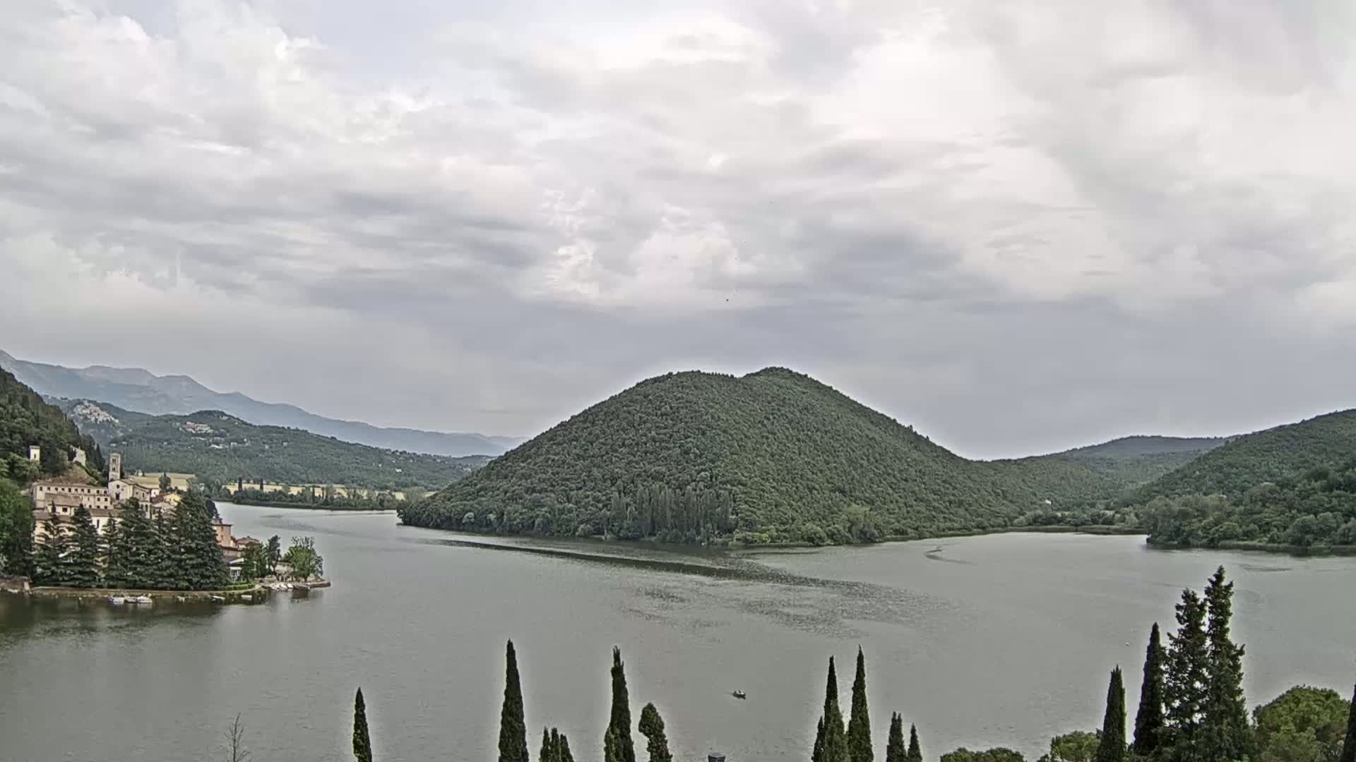 A lake surrounded by green hills and a village under an overcast sky.