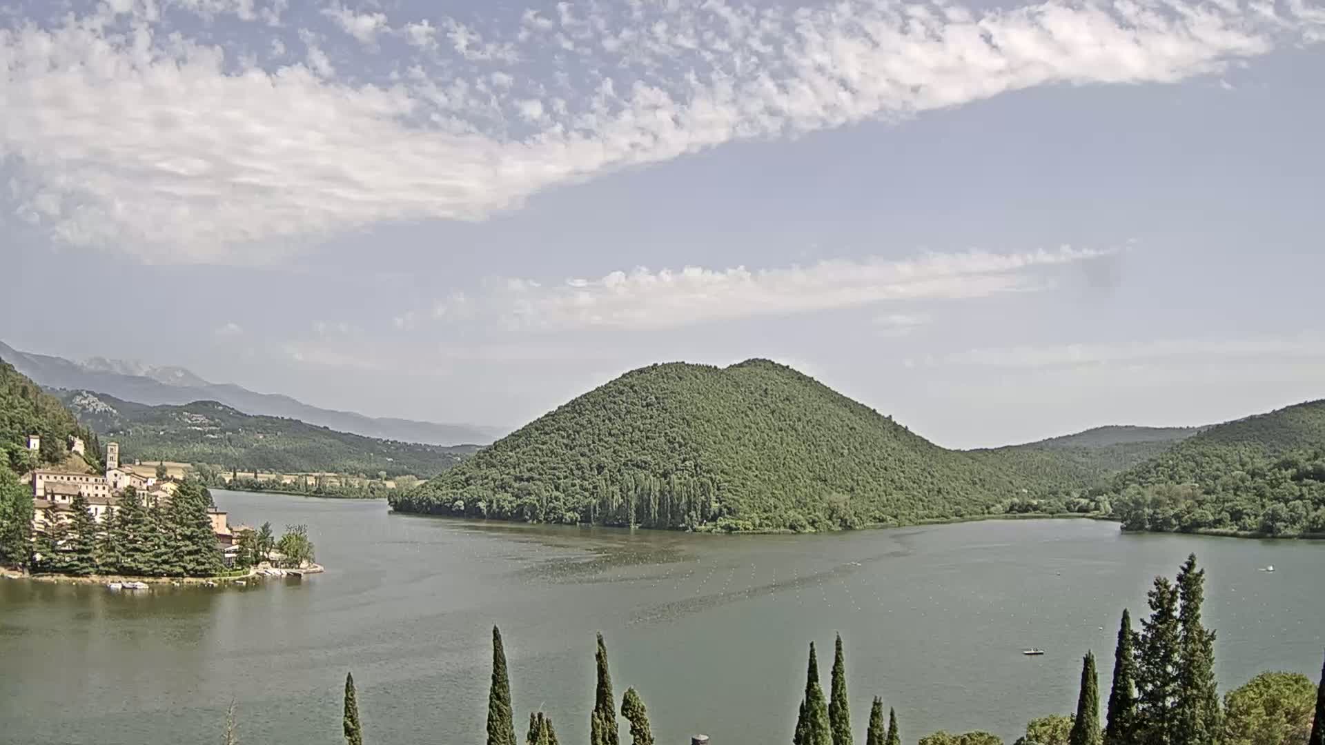 A lake surrounded by green hills and a village under a partly cloudy sky.