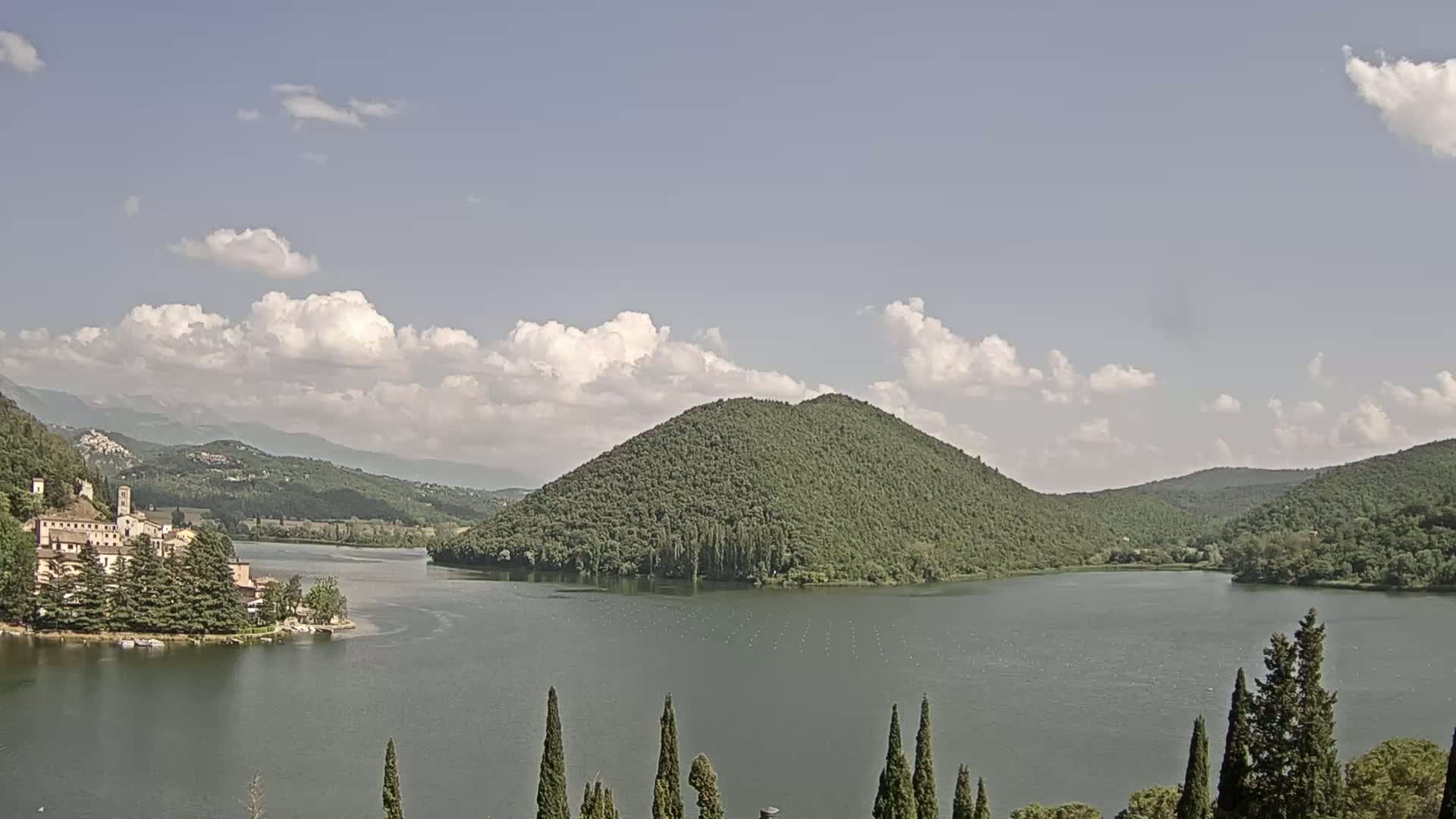 A lake surrounded by green hills and a village nestled on the shoreline under a partly cloudy sky.