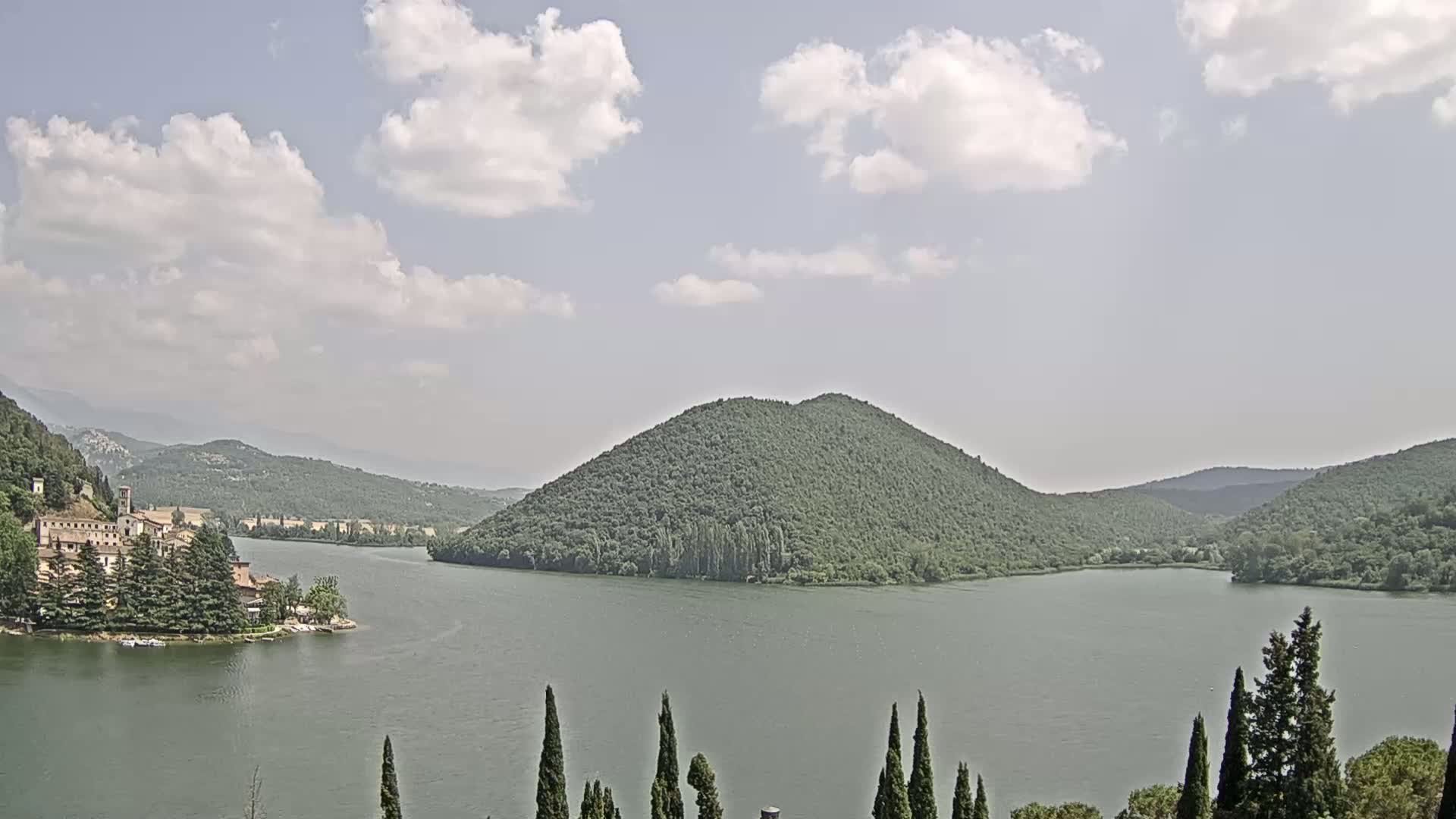 A lake surrounded by green hills and a small village under a partly cloudy sky.