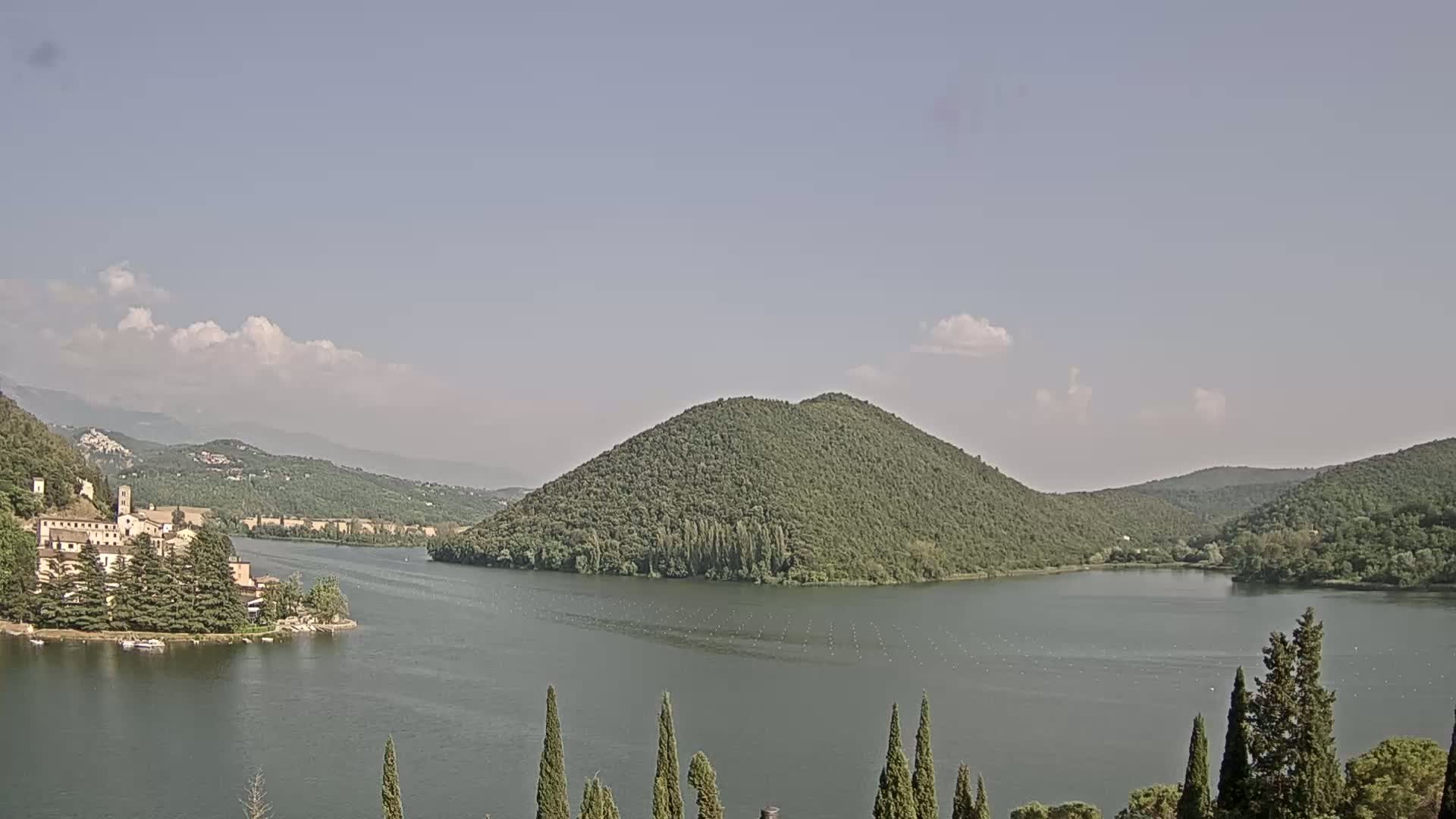 A lake surrounded by green hills and a village, under a partly cloudy sky.