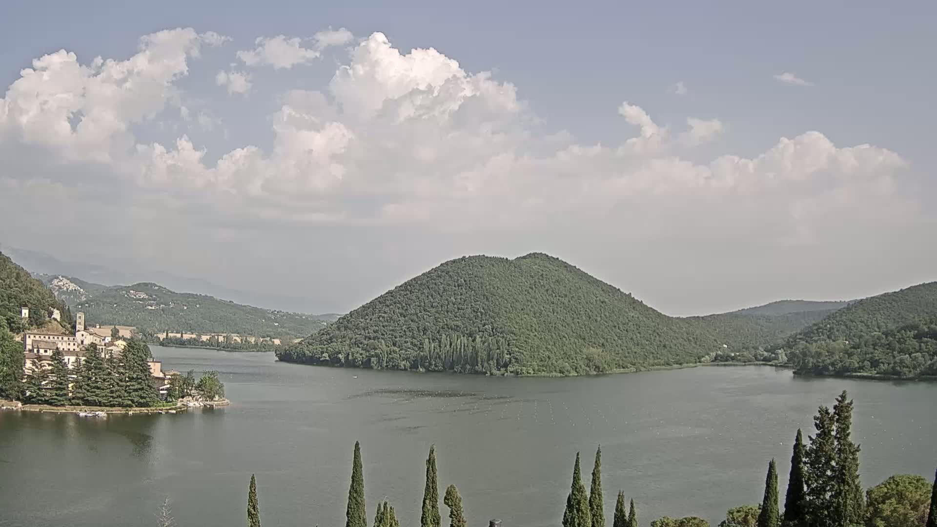 A lake surrounded by green hills and a small village under a partly cloudy sky.