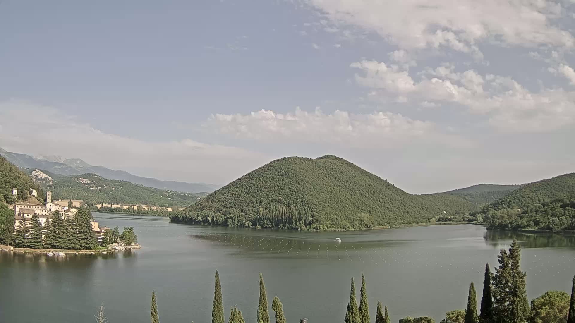 A tranquil lake nestled in a valley between verdant hills under a partly cloudy sky.