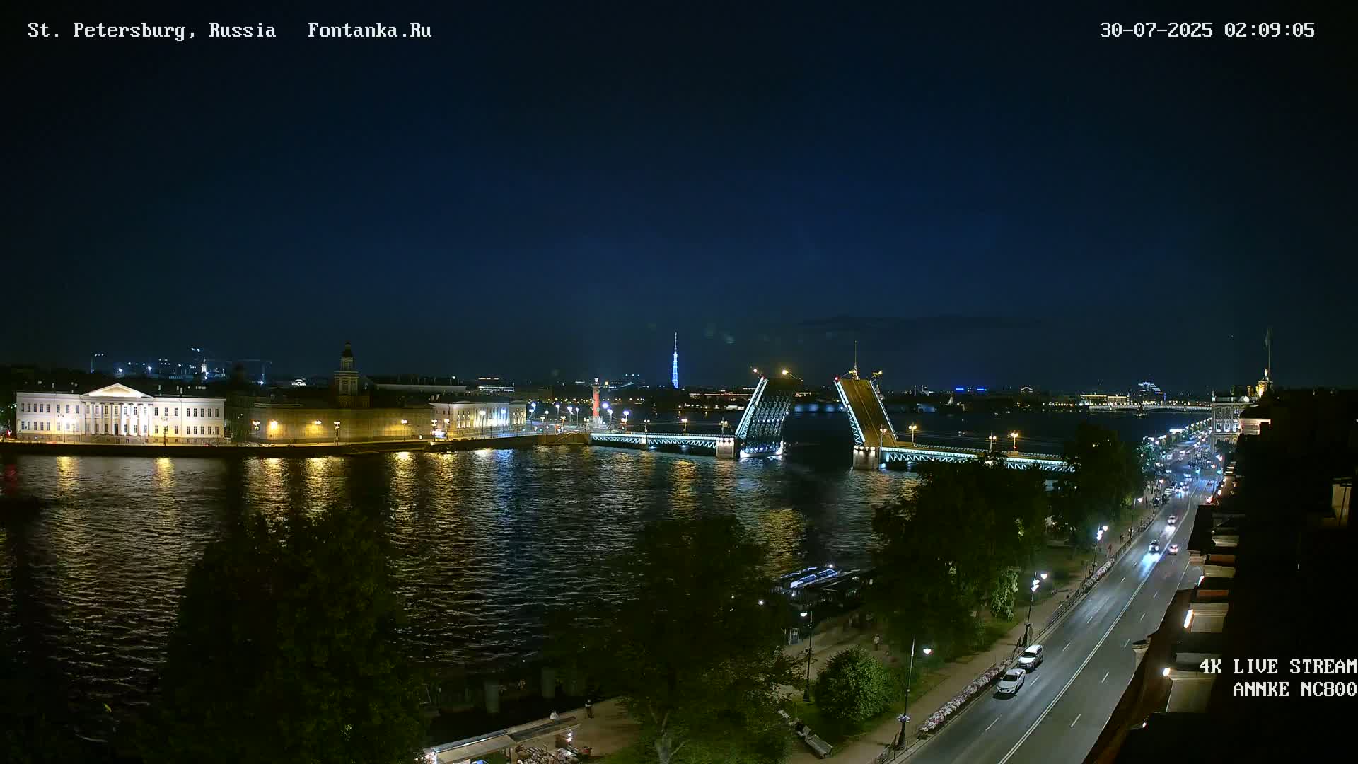 A nighttime view of a city across a river, featuring bridges, buildings, and streetlights under a clear, dark sky.