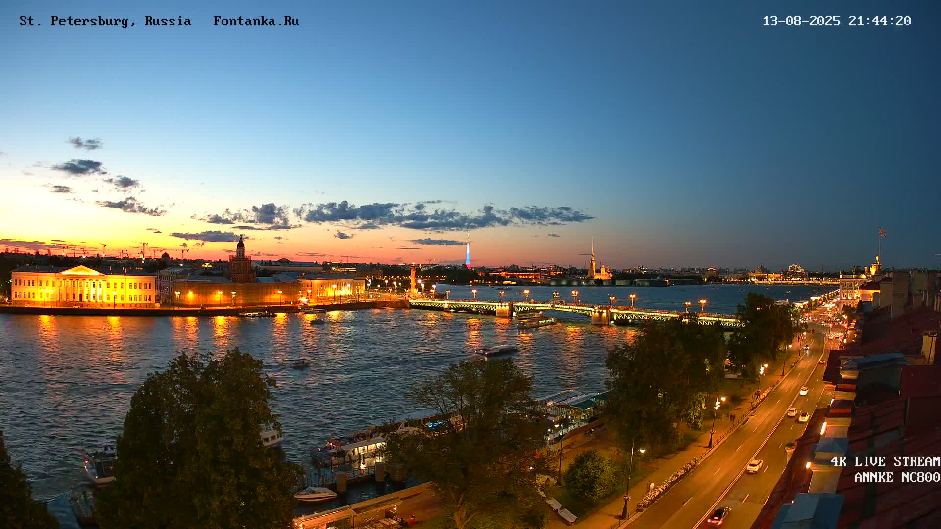 A nighttime view of a city with a river, bridges, and illuminated buildings under a twilight sky.