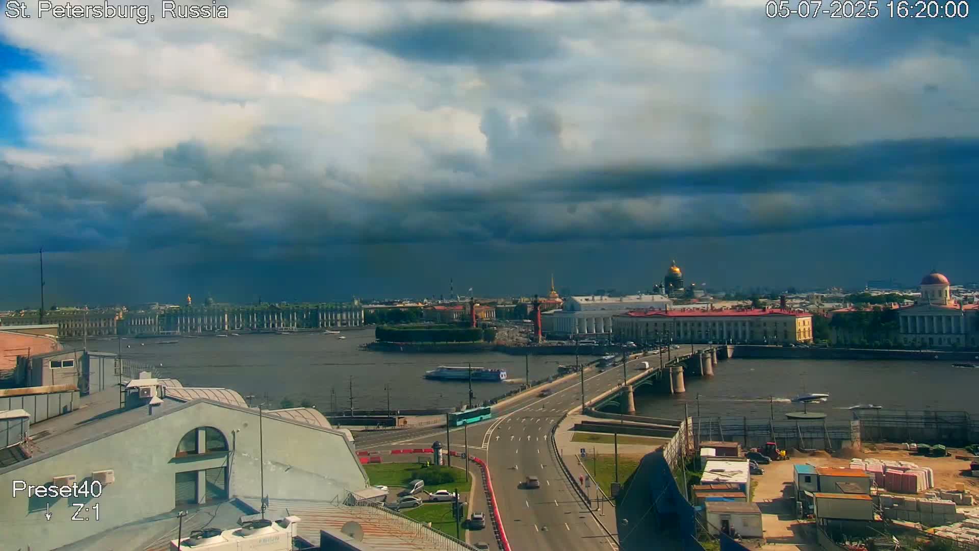 A partly cloudy sky over a river, with a bridge and cityscape visible, including several buildings and a dome.