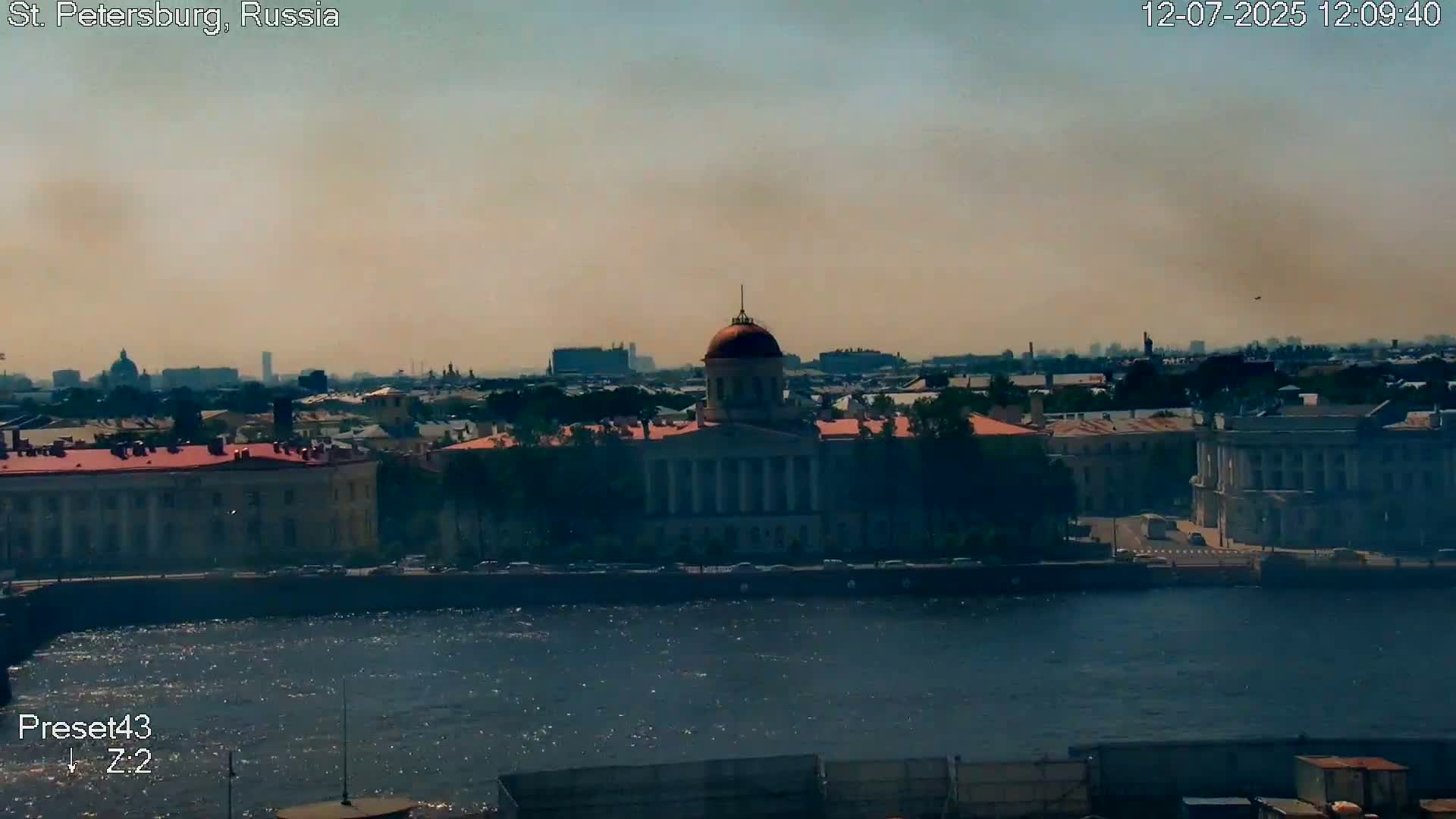 A partly cloudy sky over a river, with a bridge and cityscape visible, including several buildings and a dome.