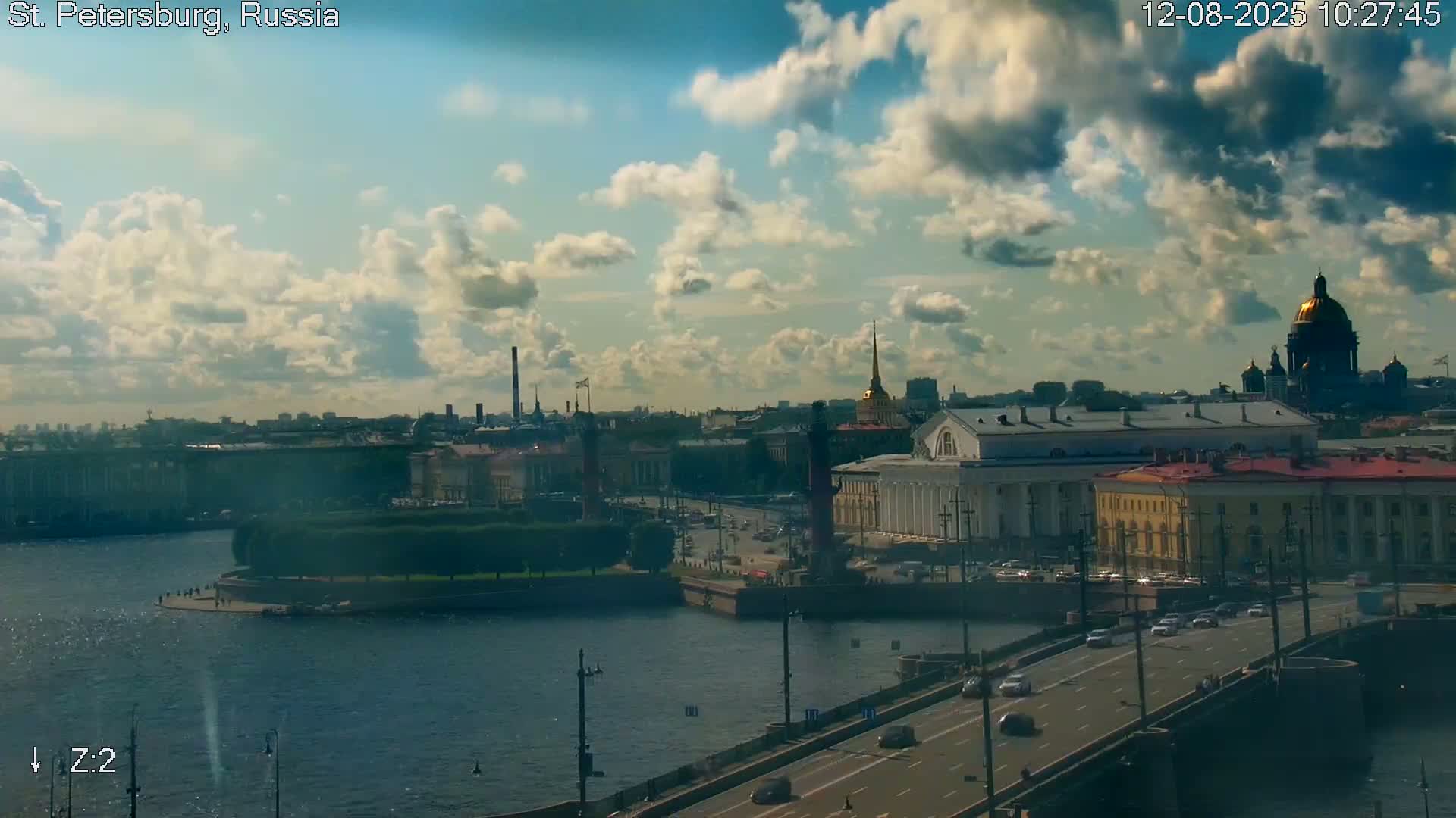 A partly cloudy sky overlooks a cityscape with a river, a bridge with cars, and several prominent buildings, including a large domed structure.