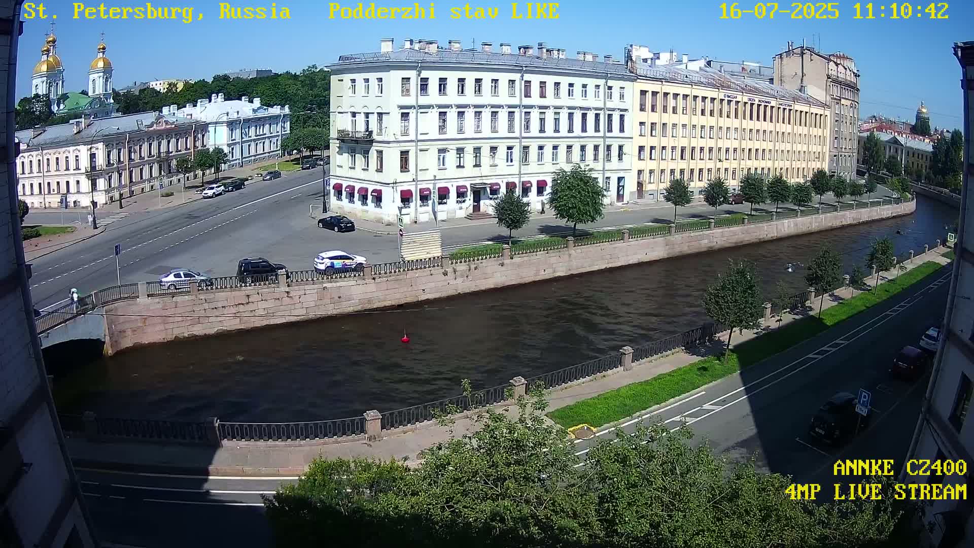 A sunny day overlooking a canal in a city with several multi-story buildings, cars on roads and a bridge.