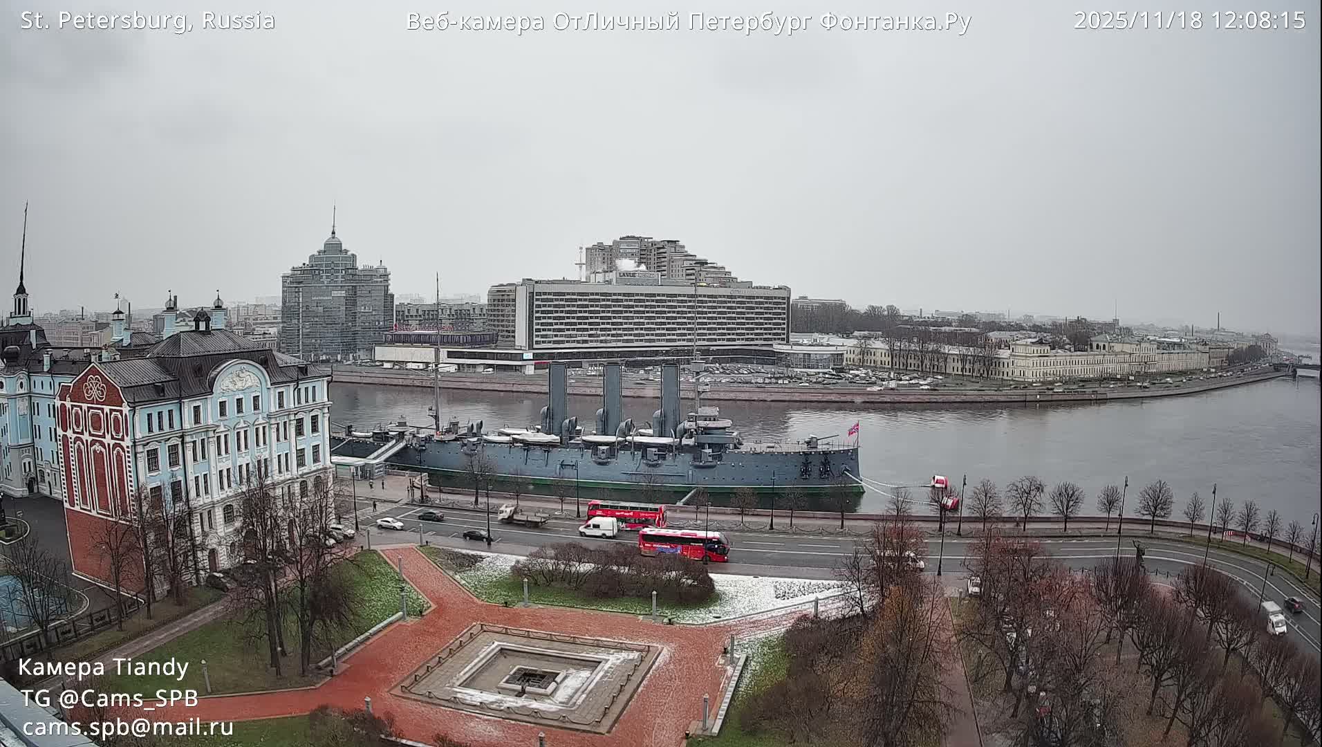 A sunny and partly cloudy winter cityscape reveals rooftops dusted with snow, golden-lit buildings, a tall modern skyscraper, and a historic sailing ship docked on a waterway.