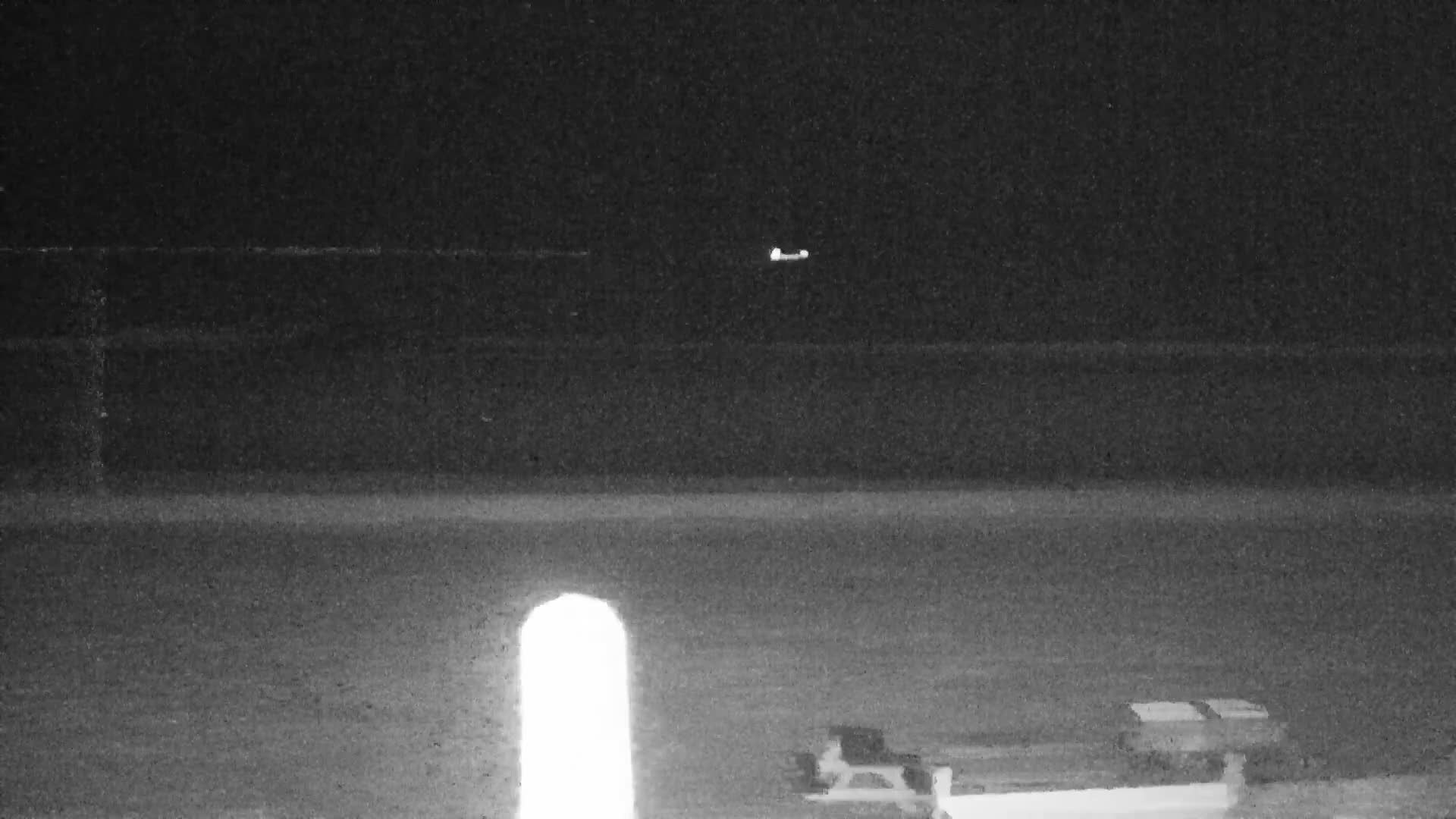 Two people stand on a wooden viewing platform overlooking a wide, sandy beach and a grey, wavy ocean under an overcast sky.