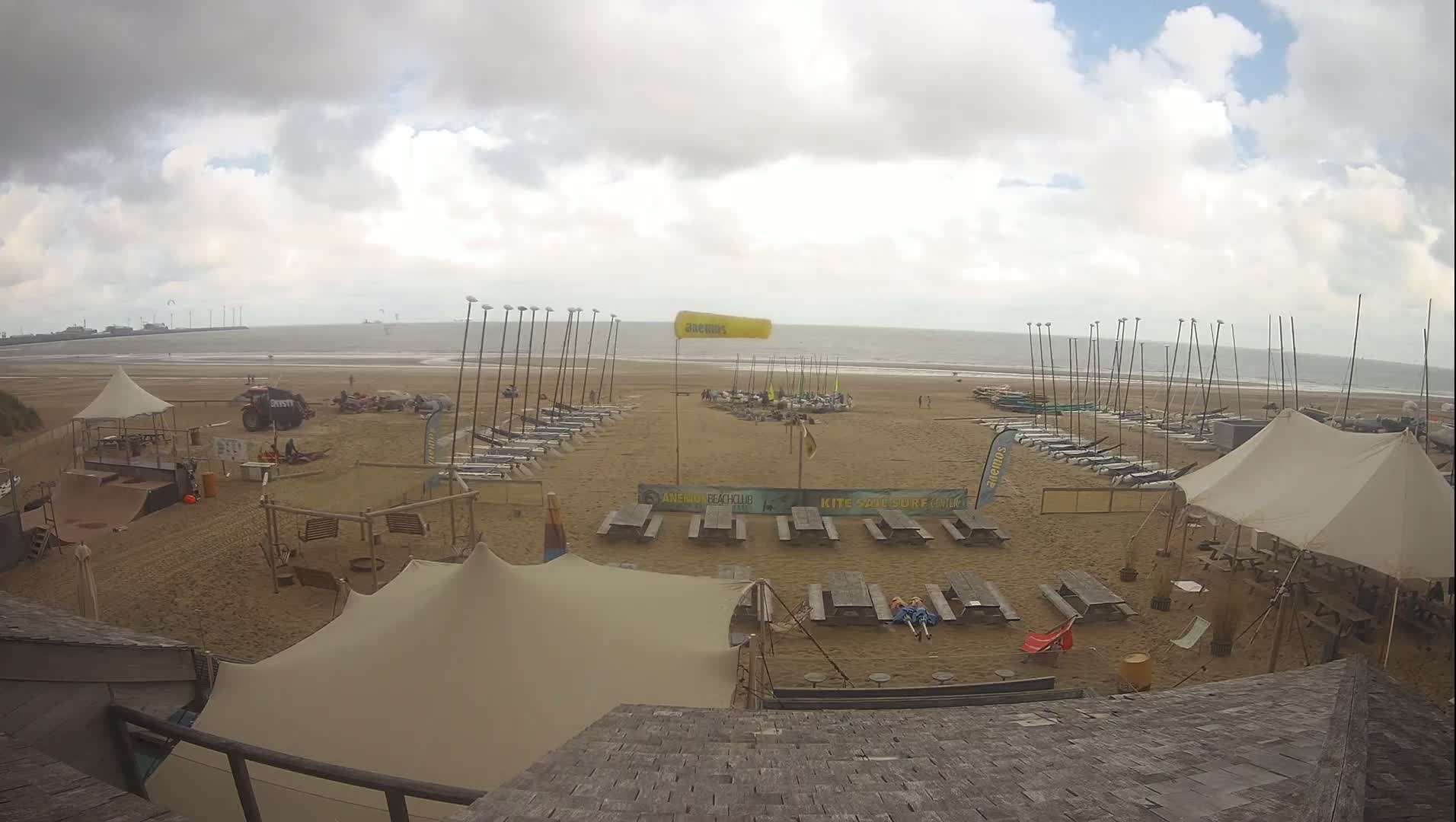 A sandy beach with numerous sailboats and tents, under a partly cloudy sky.