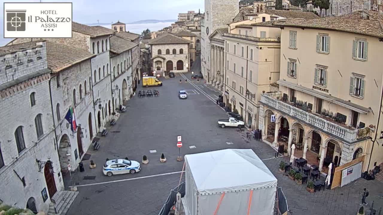 A mostly empty town square with several buildings, a few cars, and a white canopy is visible under an overcast sky.