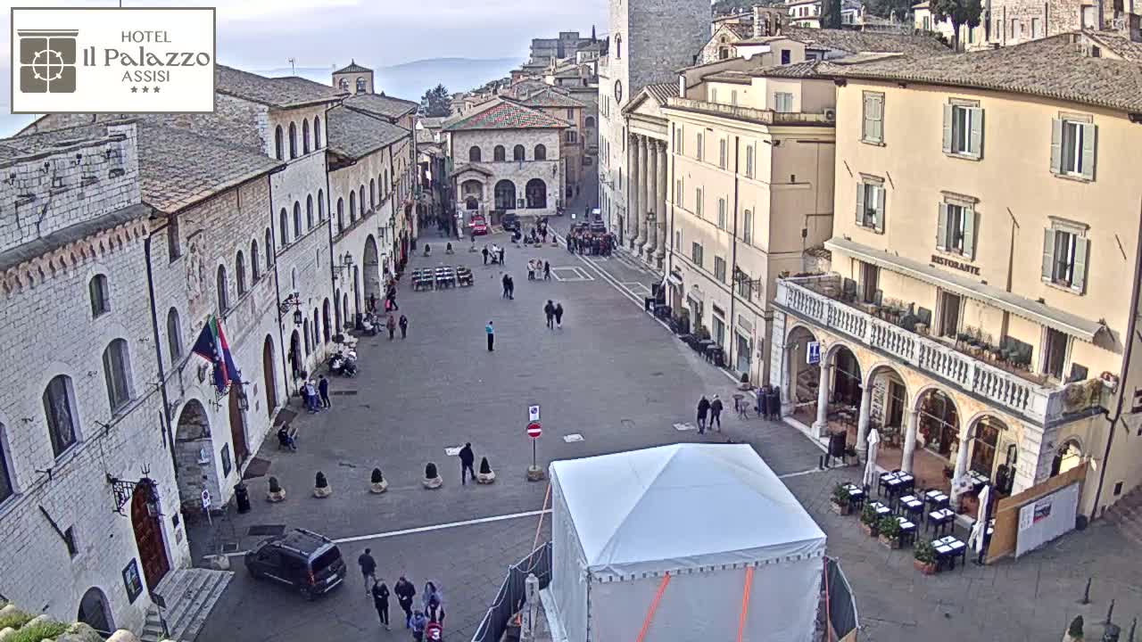 A large, mostly empty town square is surrounded by aged stone buildings under an overcast sky.