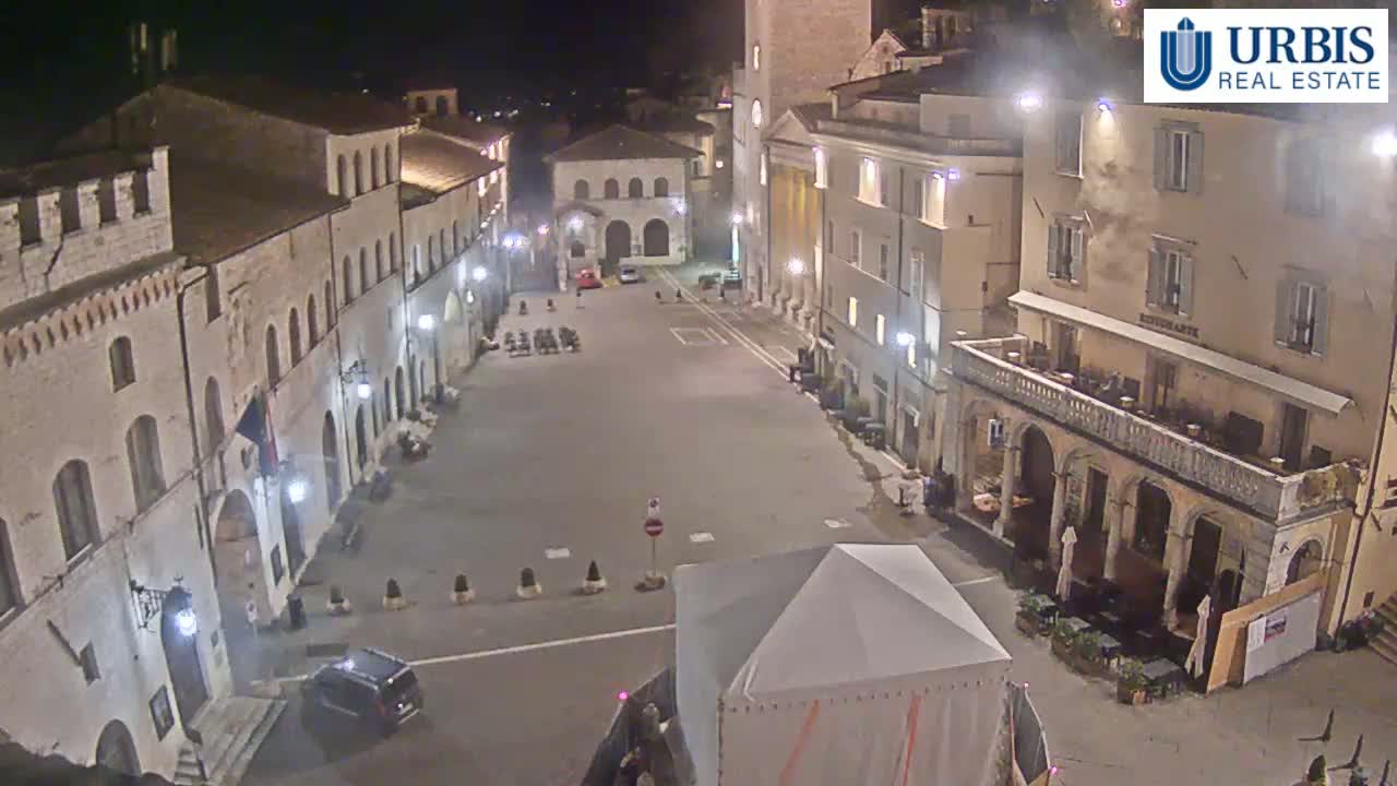 A mostly empty town square at night, surrounded by old stone buildings under clear skies.
