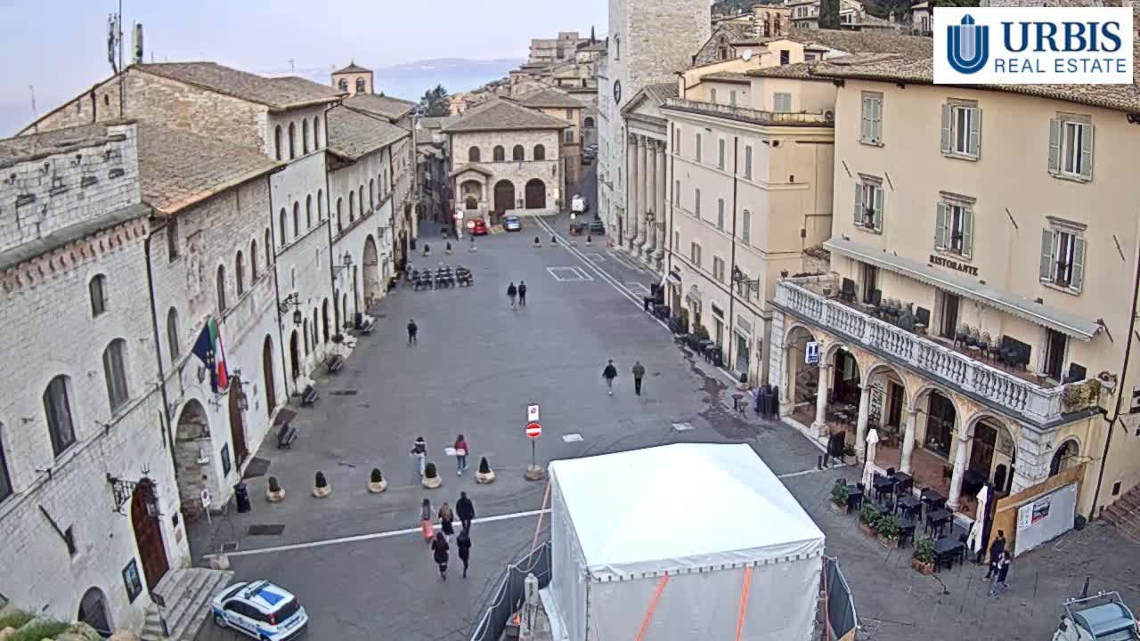 A large, empty town square is surrounded by aged stone buildings under an overcast sky.