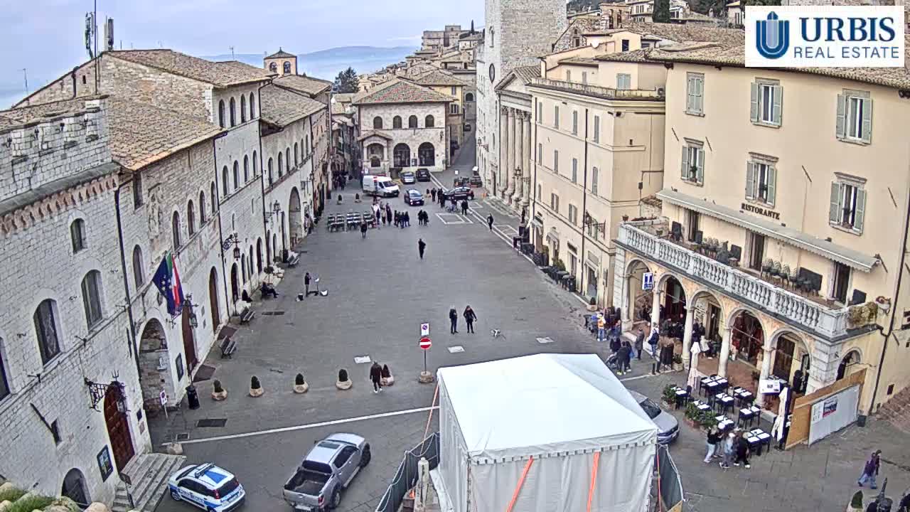 A large, mostly empty town square with several stone buildings surrounding it, under an overcast sky.