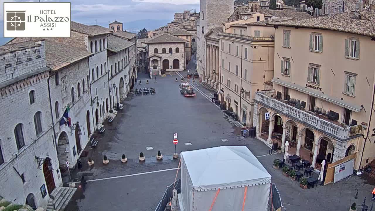 A mostly empty town square, surrounded by historic buildings, is slightly wet under an overcast sky.