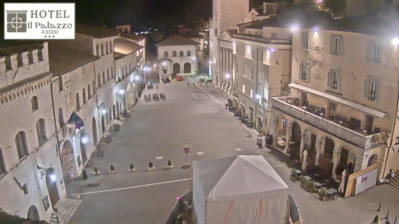 A mostly empty, brightly lit town square at night, surrounded by old stone buildings.