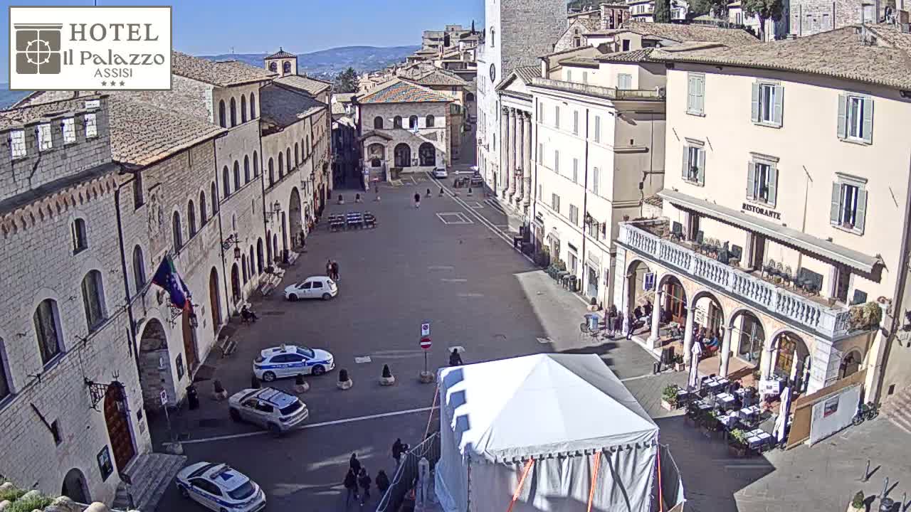 A large, mostly empty town square is surrounded by historic buildings under a bright, sunny sky.