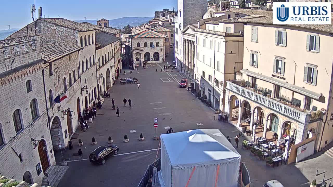 A mostly empty town square in a historic European town on a sunny day, surrounded by stone buildings.