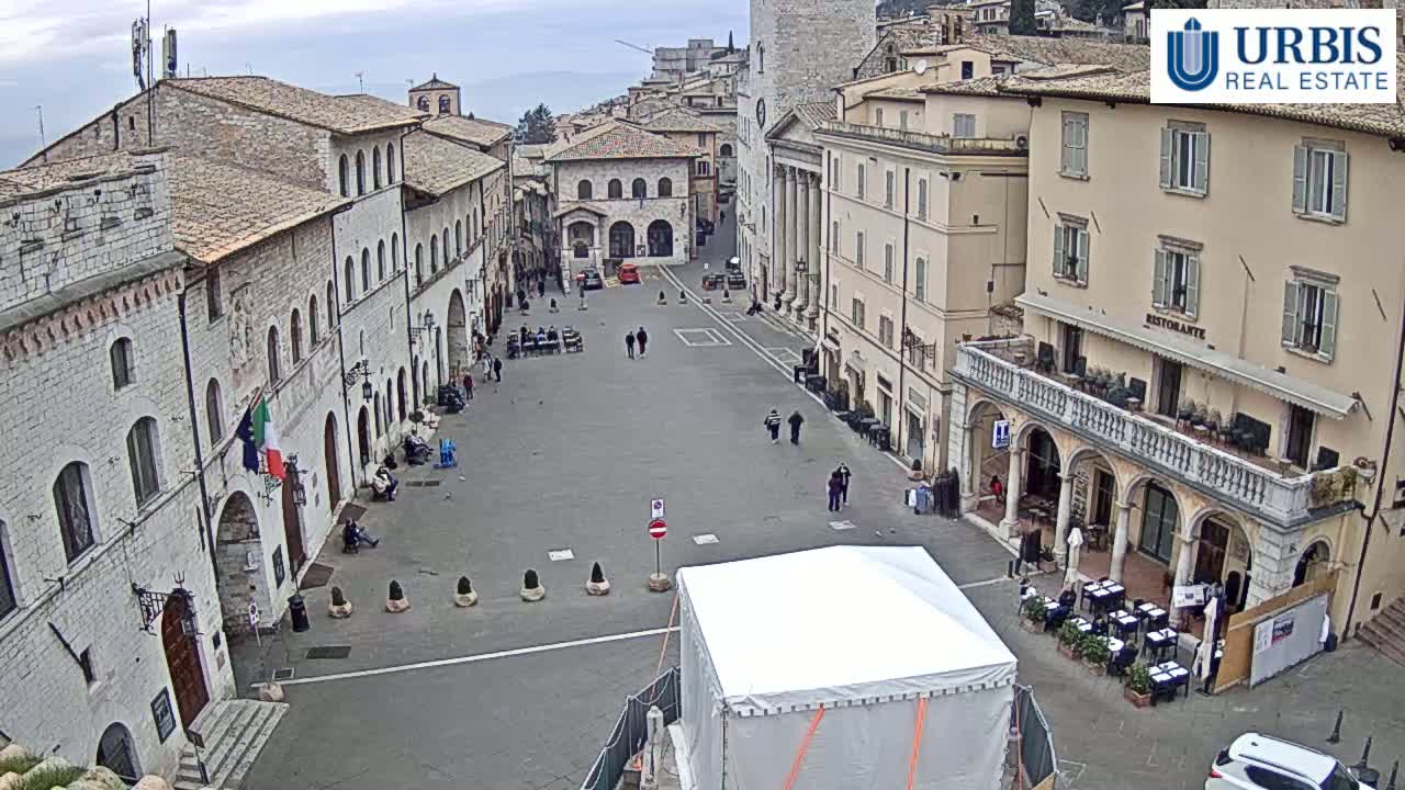 A large, mostly empty town square is surrounded by ancient-looking buildings under an overcast sky.