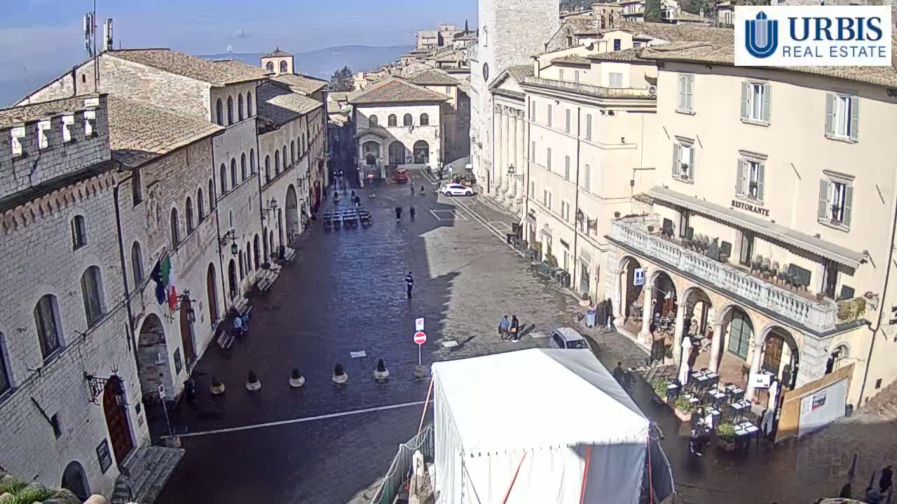 A large, mostly empty town square is surrounded by historic buildings under a clear, sunny sky.