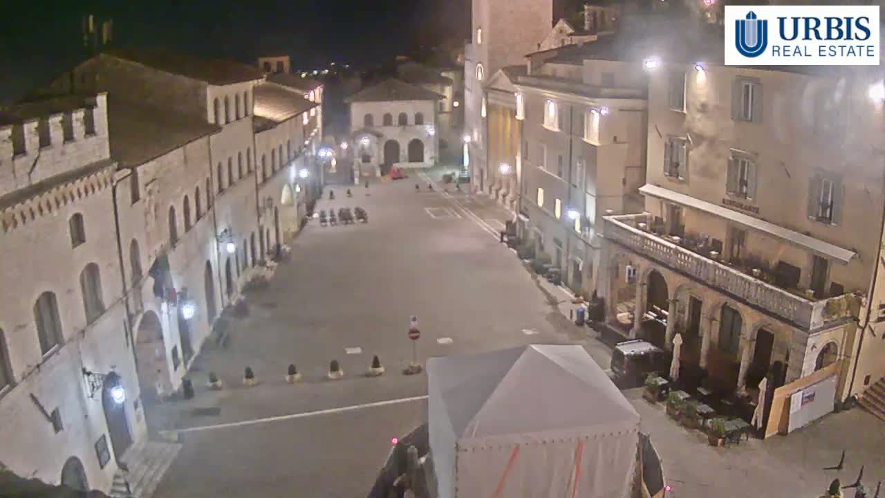 A nighttime view of a large, empty town square surrounded by historic-looking buildings under clear skies.